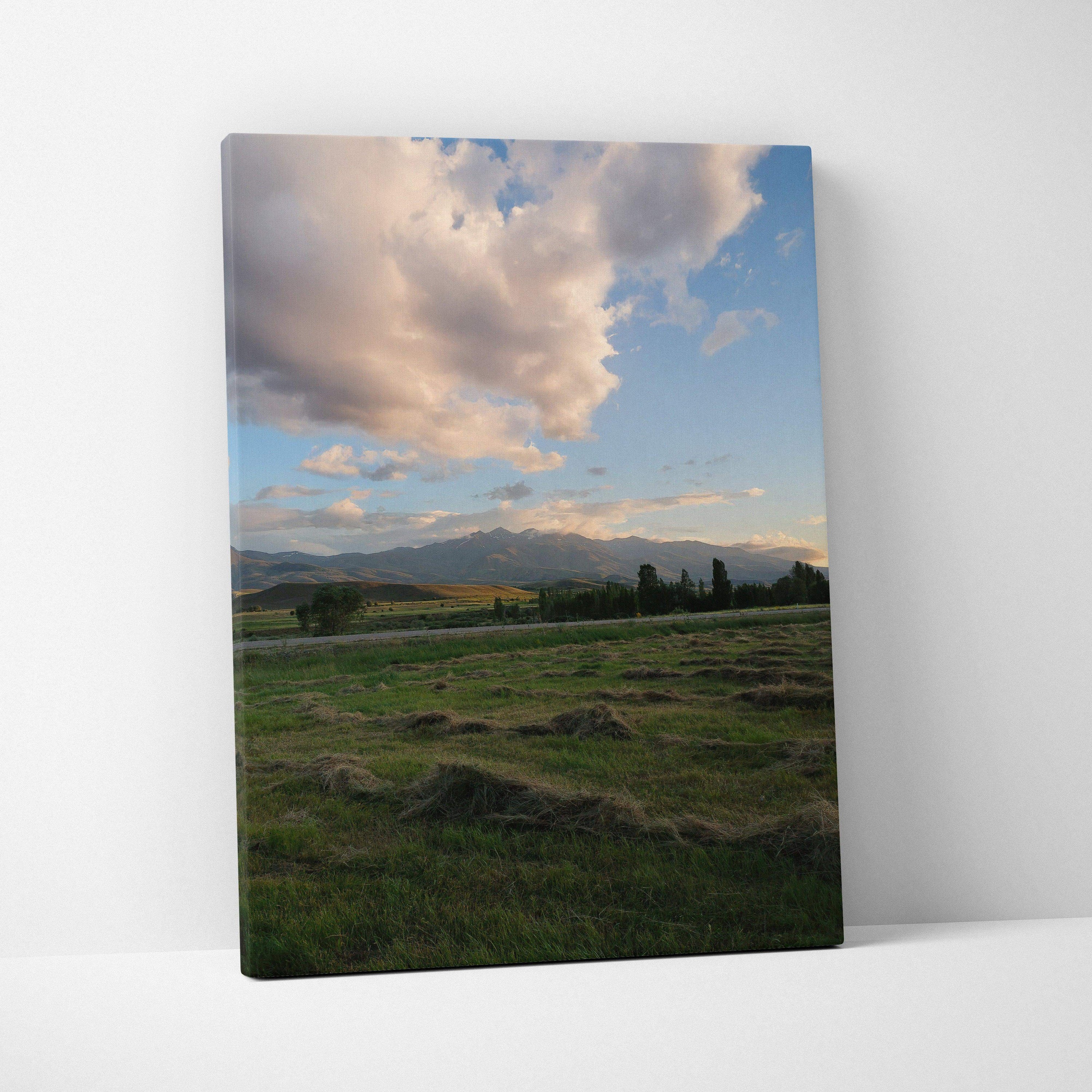 Canvas wall art featuring a mountain landscape under a dramatic cloudy sky at sunset with green fields in the foreground.
