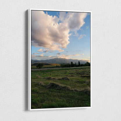 Vertical canvas wall art featuring a mountain sunset with dramatic clouds over a green field.