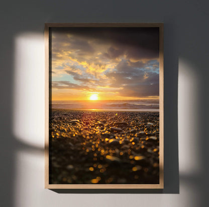 Vertical wall art poster of ocean sunset with golden light reflecting on pebbled beach.