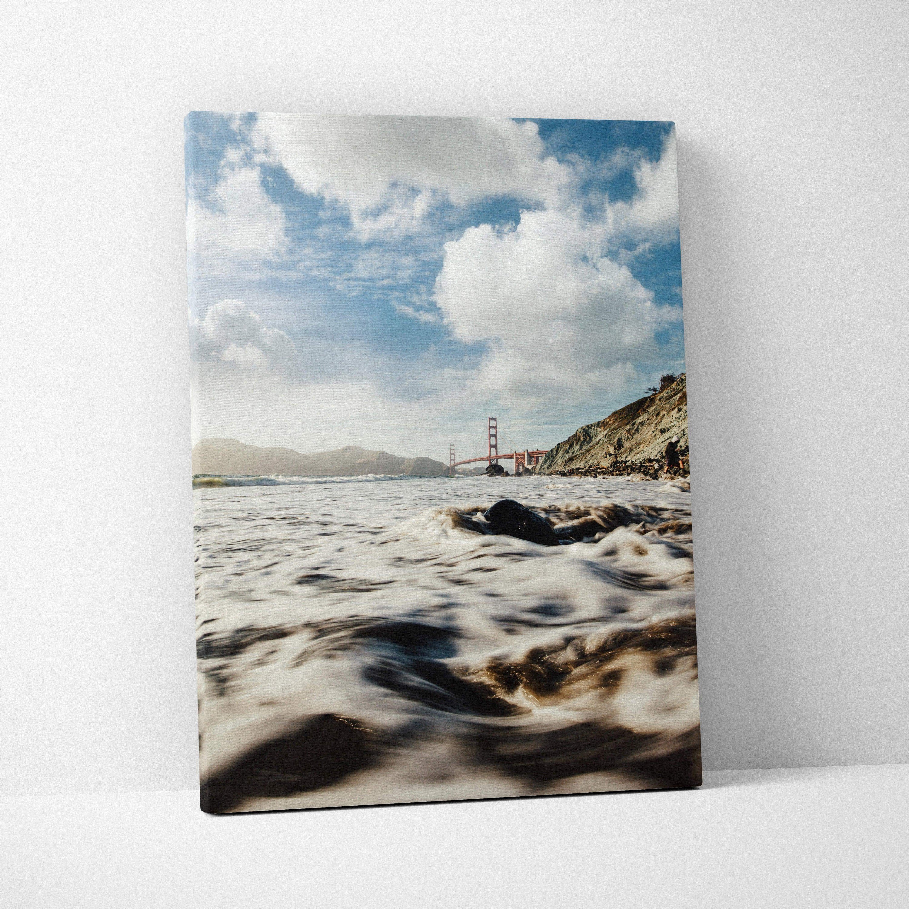 Canvas wall art of a serene beach with waves and the Golden Gate Bridge under a cloudy sky.