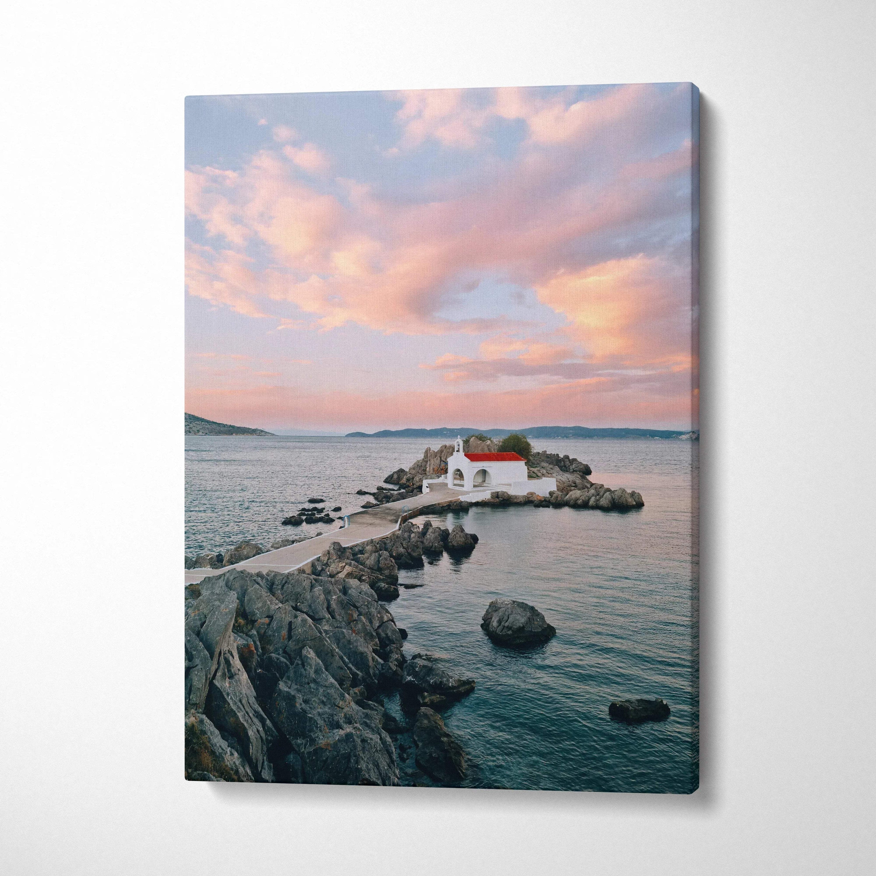 Serene sunset over rocky beach with small white building on canvas wall art.