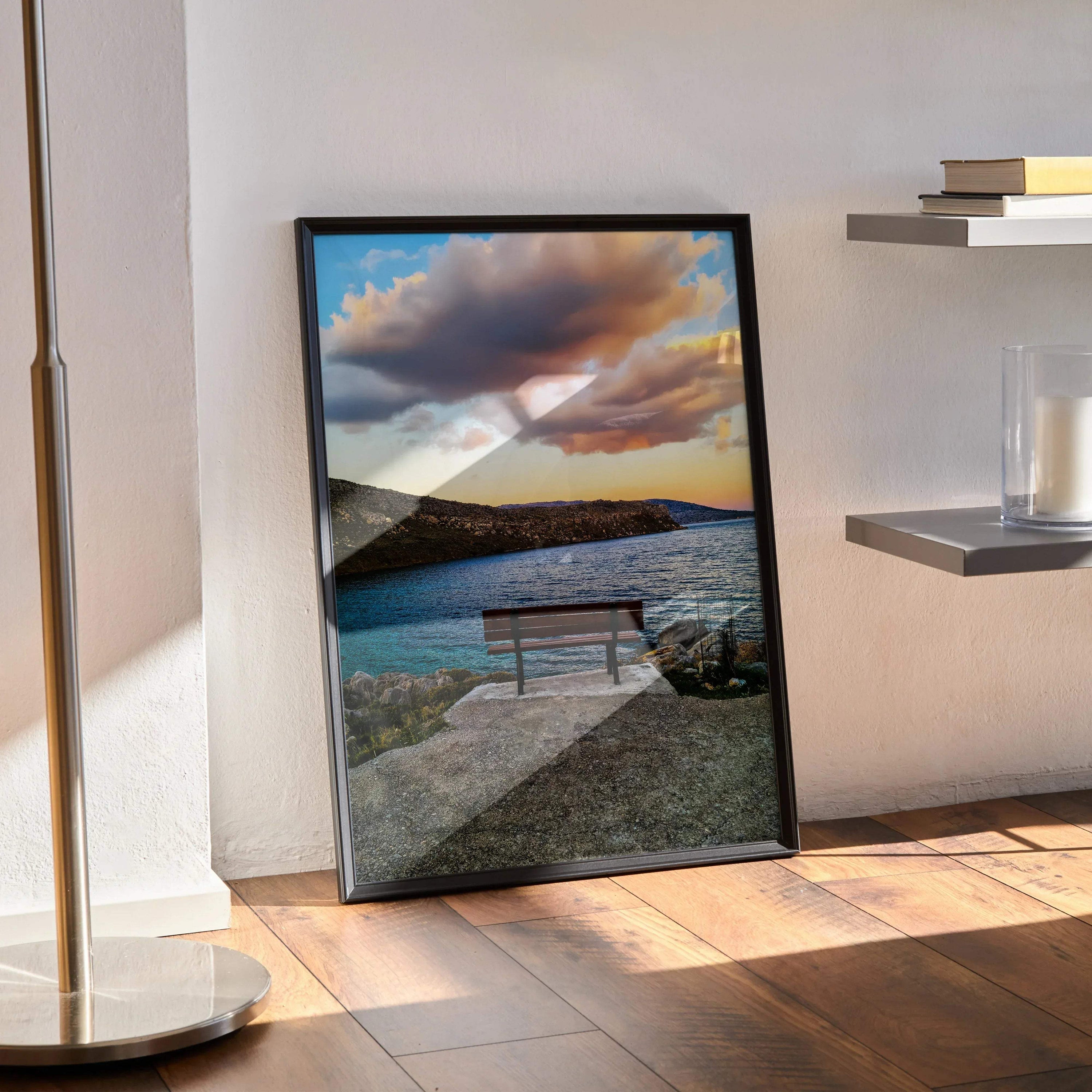 Vibrant sunset landscape poster with bench by calm water, framed wall art leaning on floor.