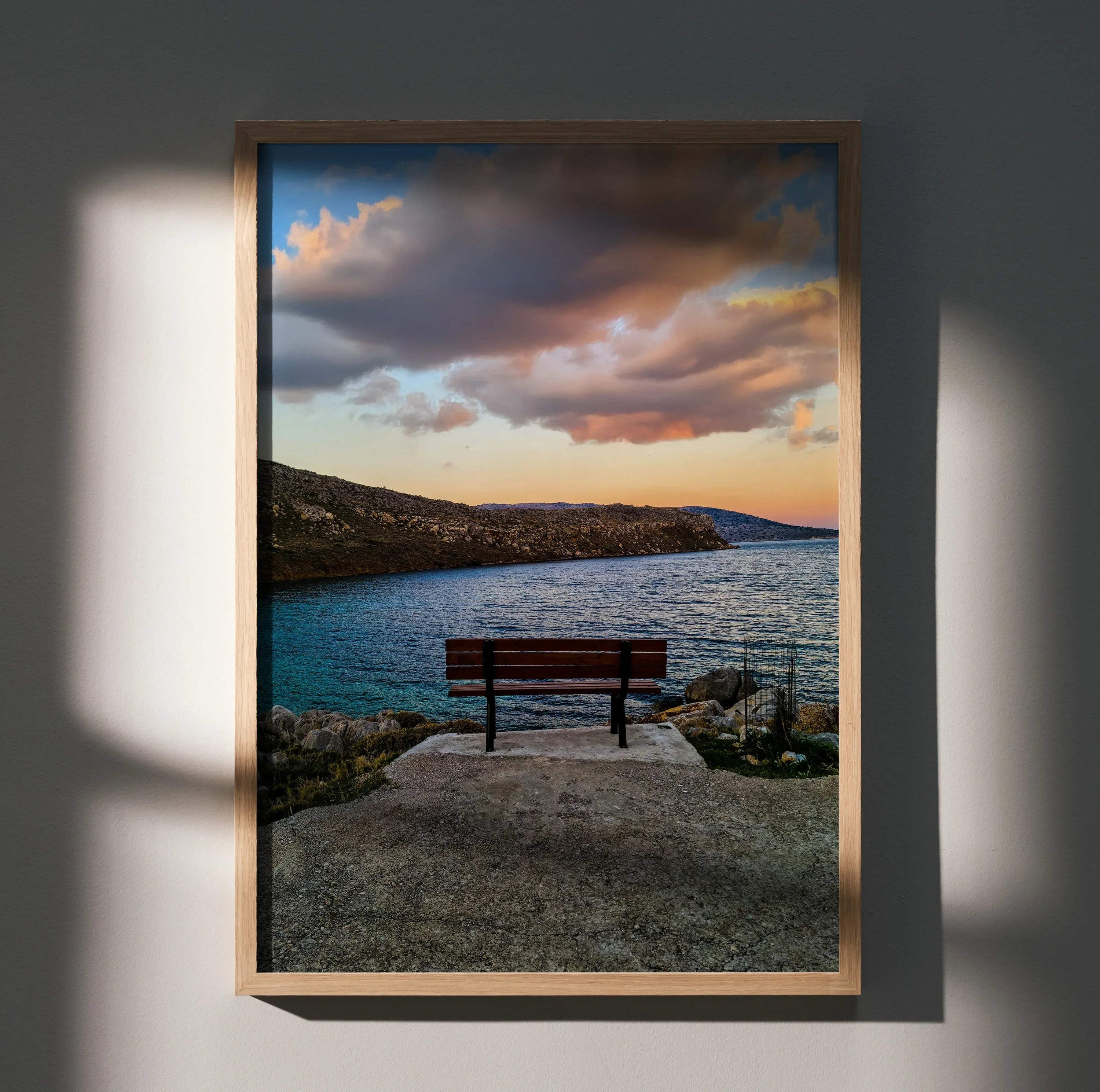 Vibrant sunset landscape poster with bench by rocky shoreline, vertical wall art.