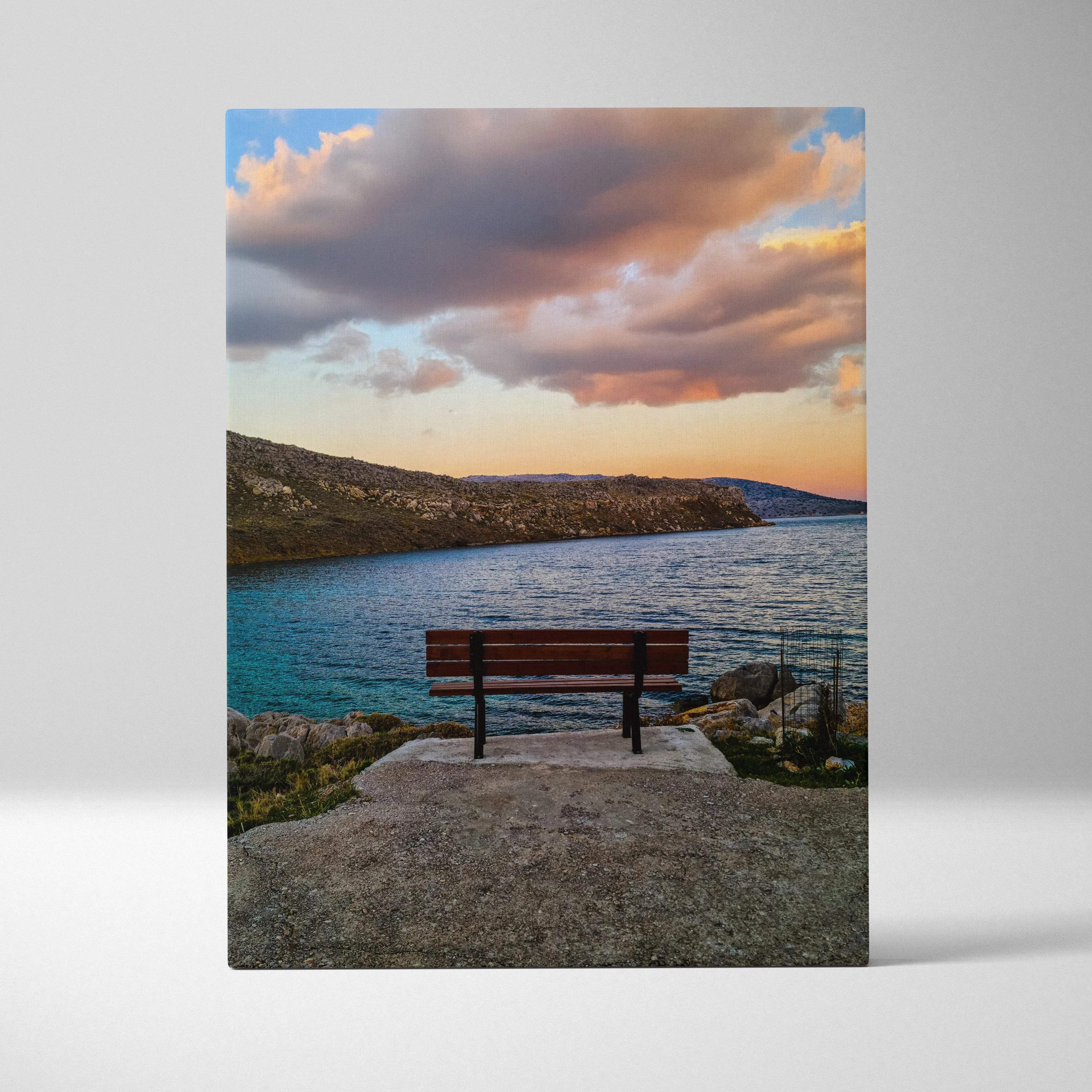 A rustic wooden bench with black metal legs on a stone platform overlooking turquoise water in tranquil sunset canvas art