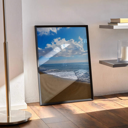 Vibrant beach ocean waves poster in black frame leaning against wall, natural light on wood floor wall art.