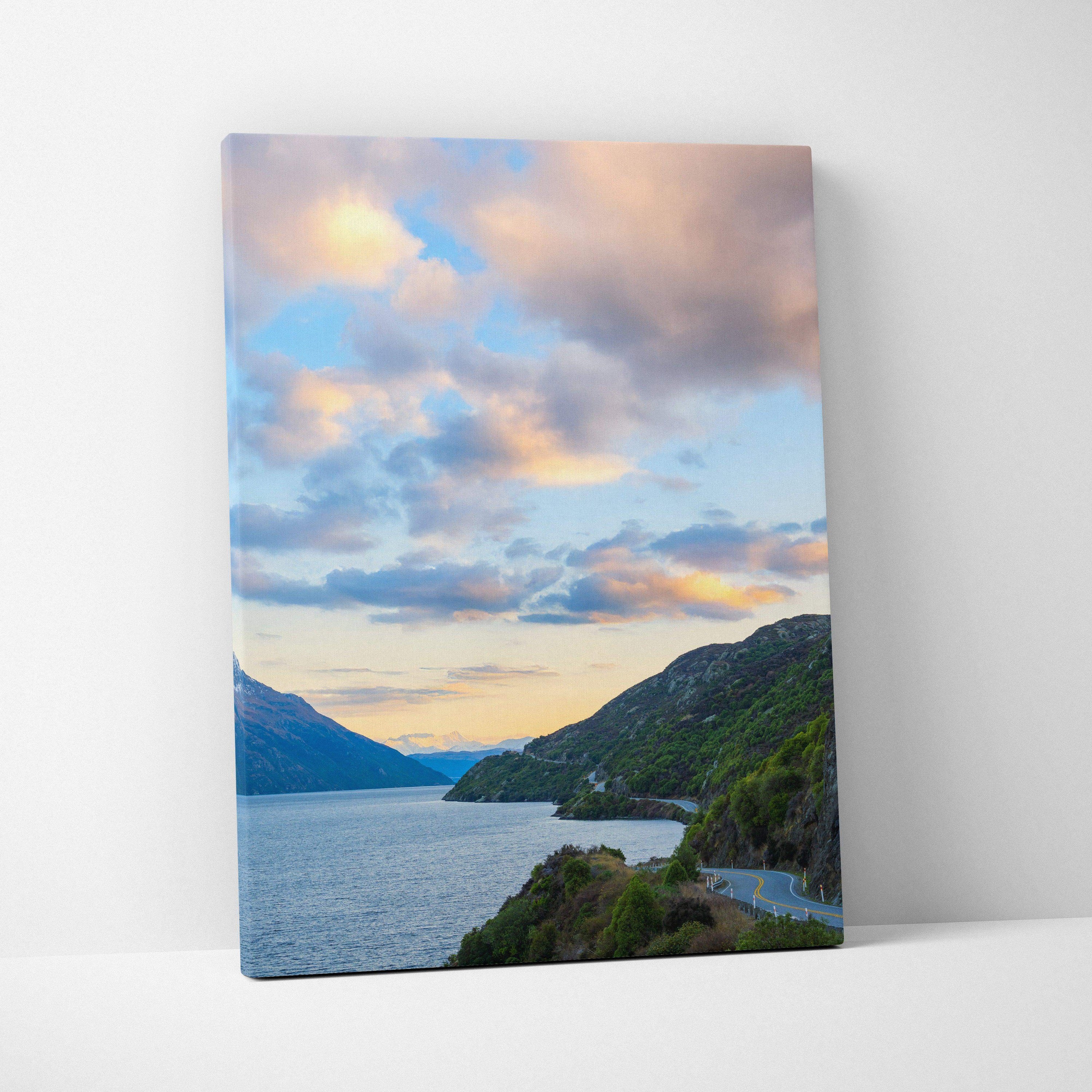 Vertical canvas wall art featuring a mountain sunset over a lake with colorful clouds and lush greenery.
