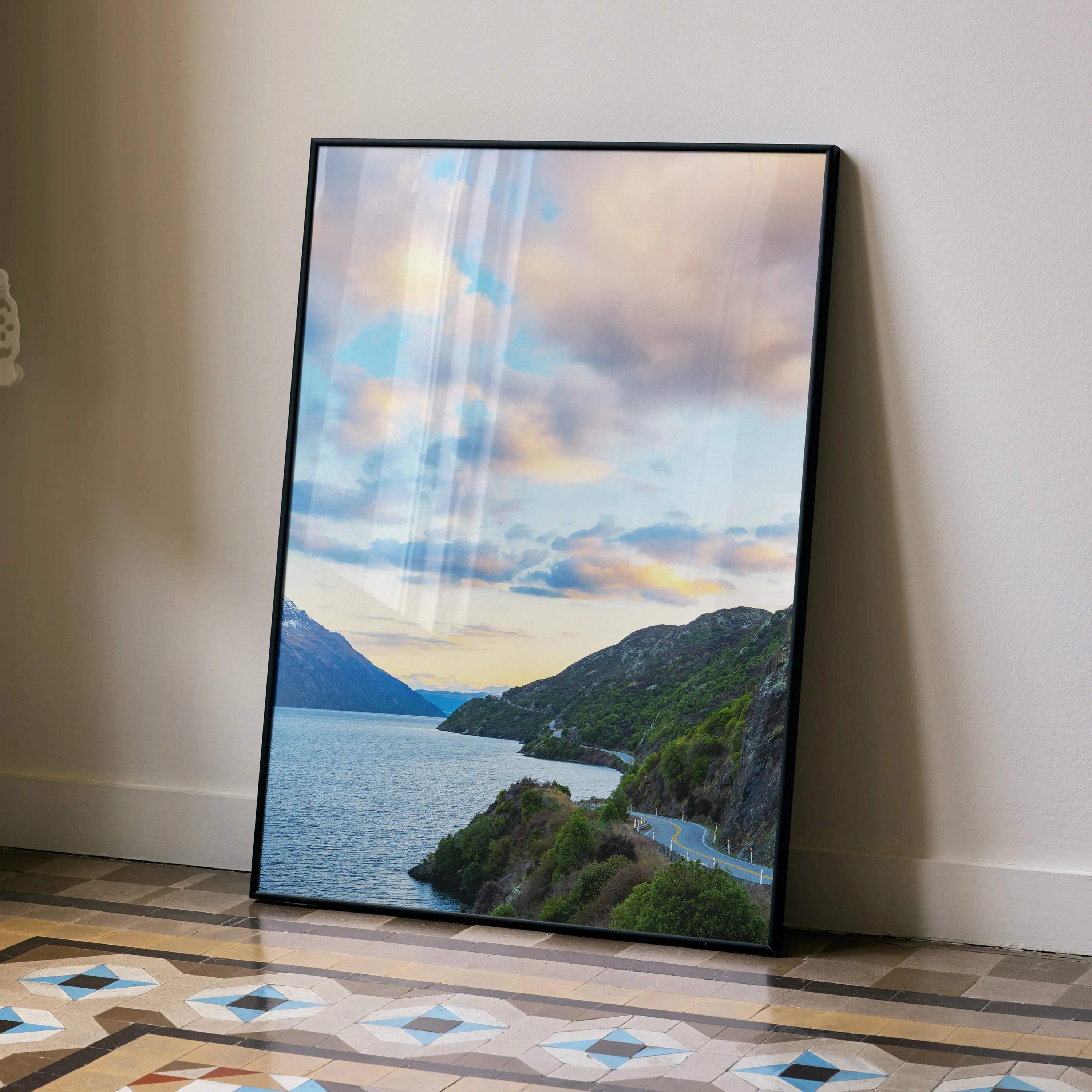 Vertical poster wall art featuring vibrant mountains and a colorful sunset sky over a winding lakeside road.