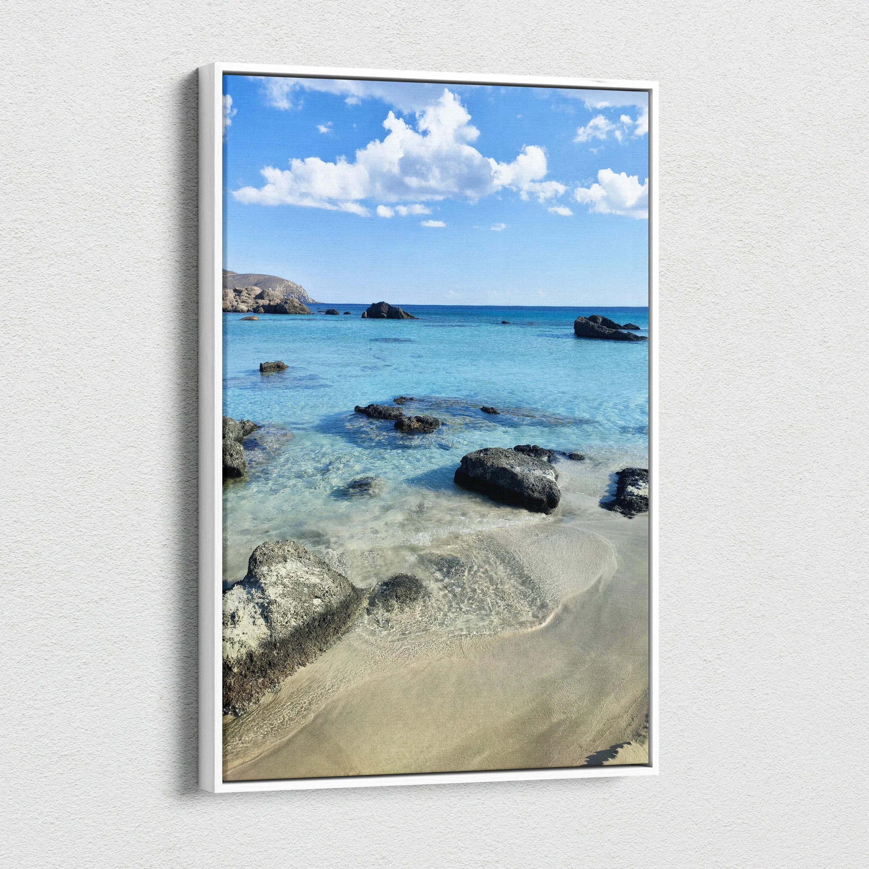 Vertical canvas wall art featuring a serene beach scene with clear blue water, rocks, and a bright sky.