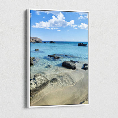 Vertical canvas wall art featuring a serene beach scene with clear blue water, rocks, and a bright sky.
