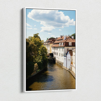 Vertical canvas wall art featuring urban buildings alongside a river under a partly cloudy sky.