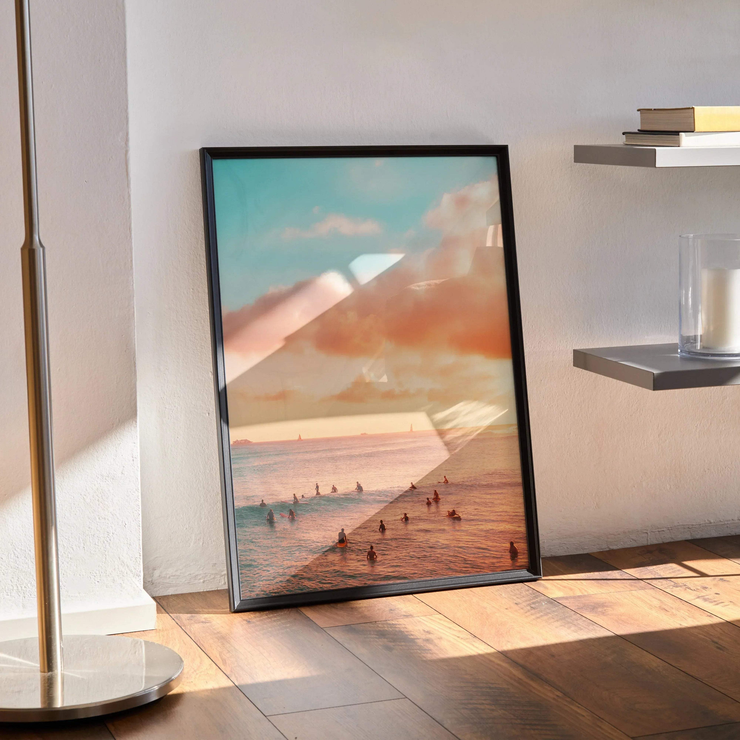 Ocean sunset poster with warm orange sky and silhouetted beach figures in black frame leaning on wall.
