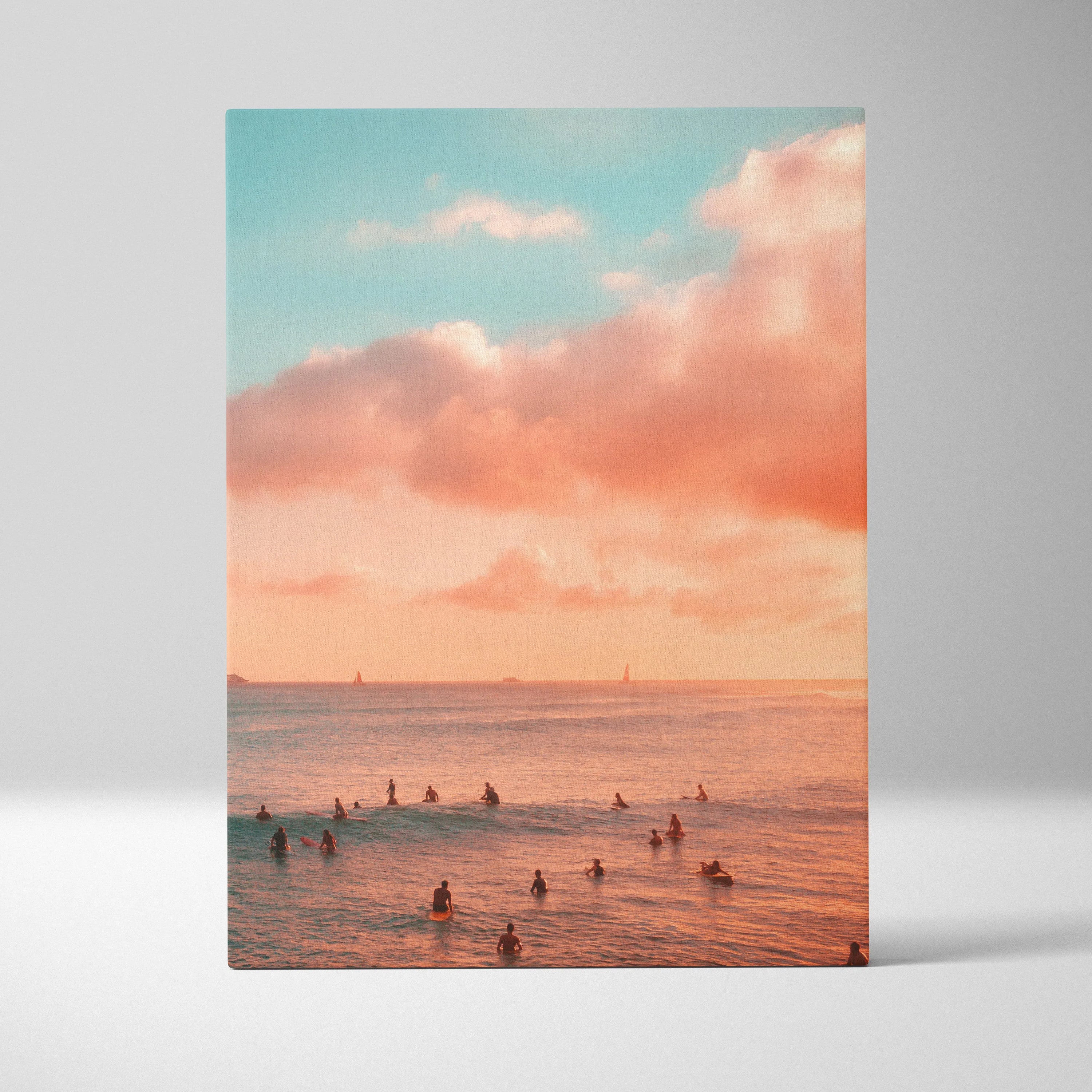 Vertical canvas wall art depicting a golden sunset over ocean waves with swimmers in the water and soft pink clouds above.
