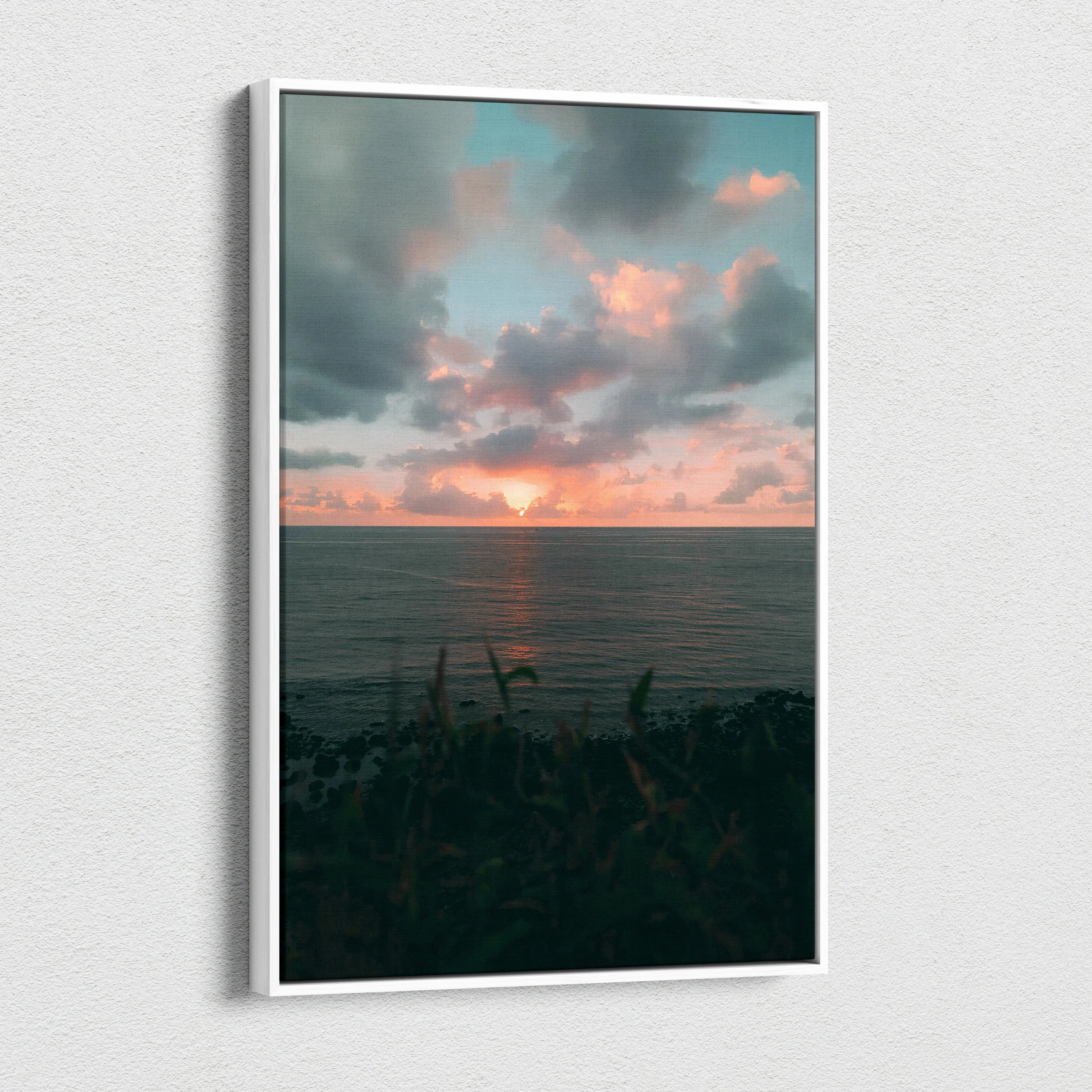Vertical canvas wall art featuring a vibrant beach sunset over a calm ocean with dark foreground foliage.