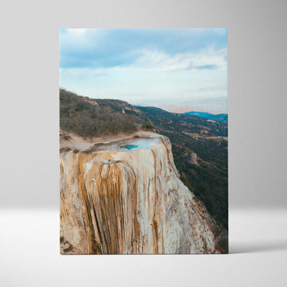 Vertical canvas wall art featuring a mountain cliff with blue pools and a cloudy sky at sunset.