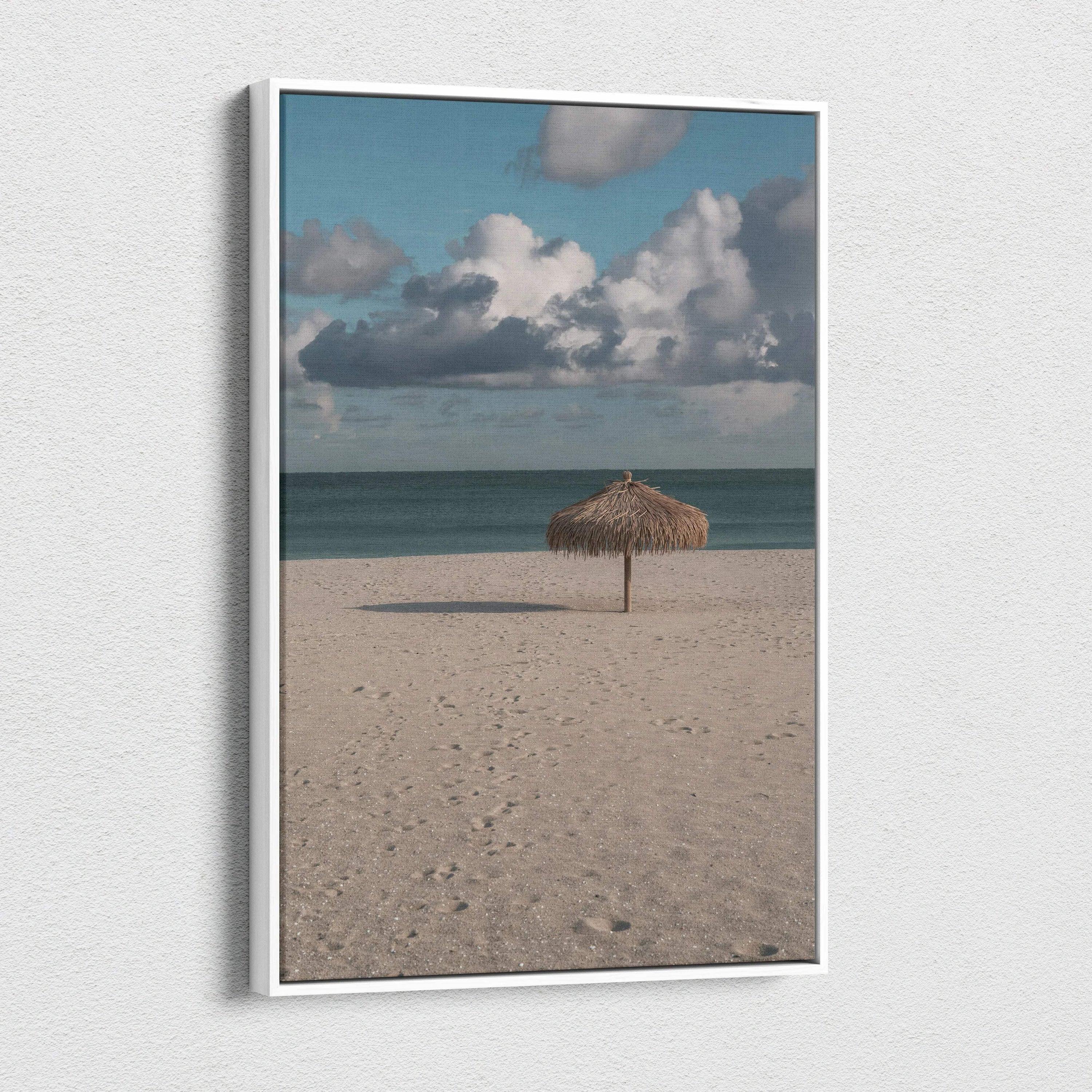 Vertical canvas wall art featuring a tranquil beach scene with a single thatched umbrella under a cloudy sky.