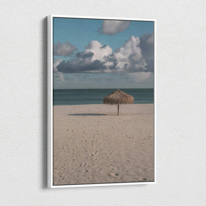 Vertical canvas wall art featuring a tranquil beach scene with a single thatched umbrella under a cloudy sky.