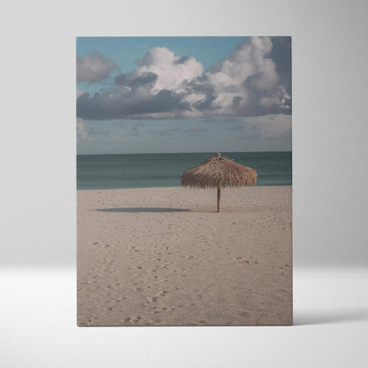 Vertical canvas wall art of tranquil beach with lone thatched umbrella under cloudy sky.