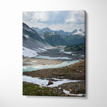 Vertical canvas wall art featuring a mountain landscape with snow patches and a tranquil alpine lake.