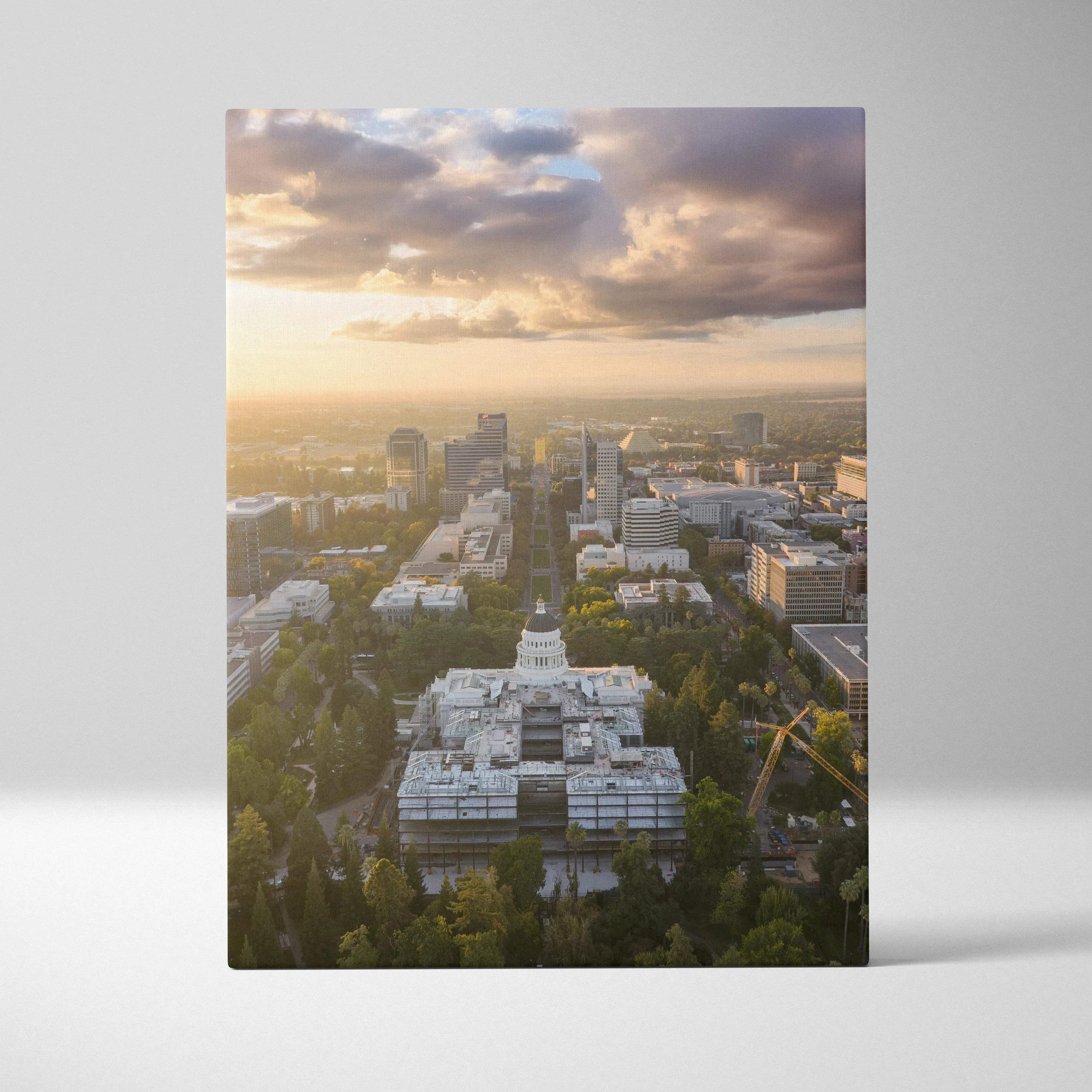 A rectangular canvas print of an aerial cityscape at sunset featuring the white domed capitol building and warm golden hour glow