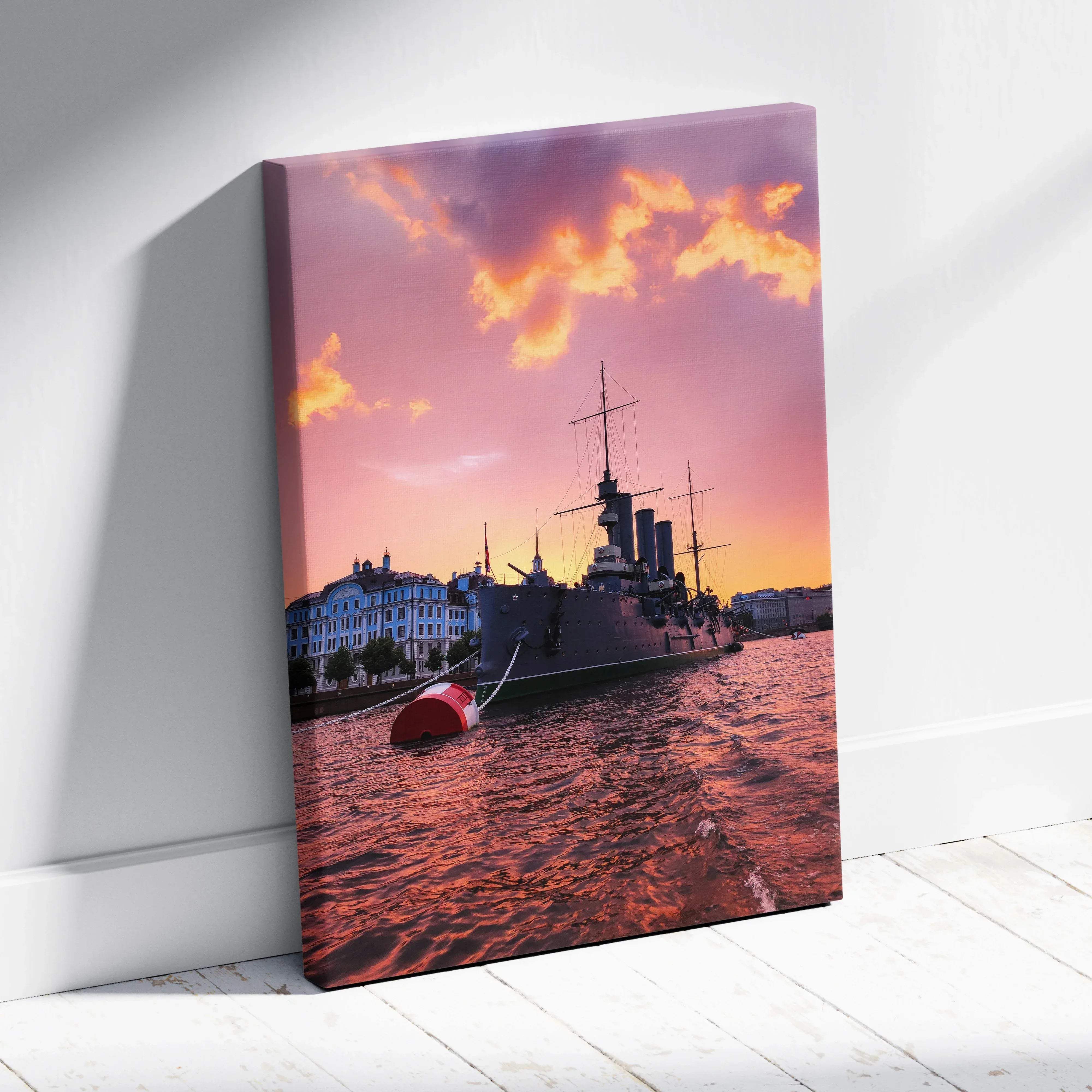 A canvas print of a dark-hulled battleship at sunset with vibrant pink and orange sky and city buildings in the background