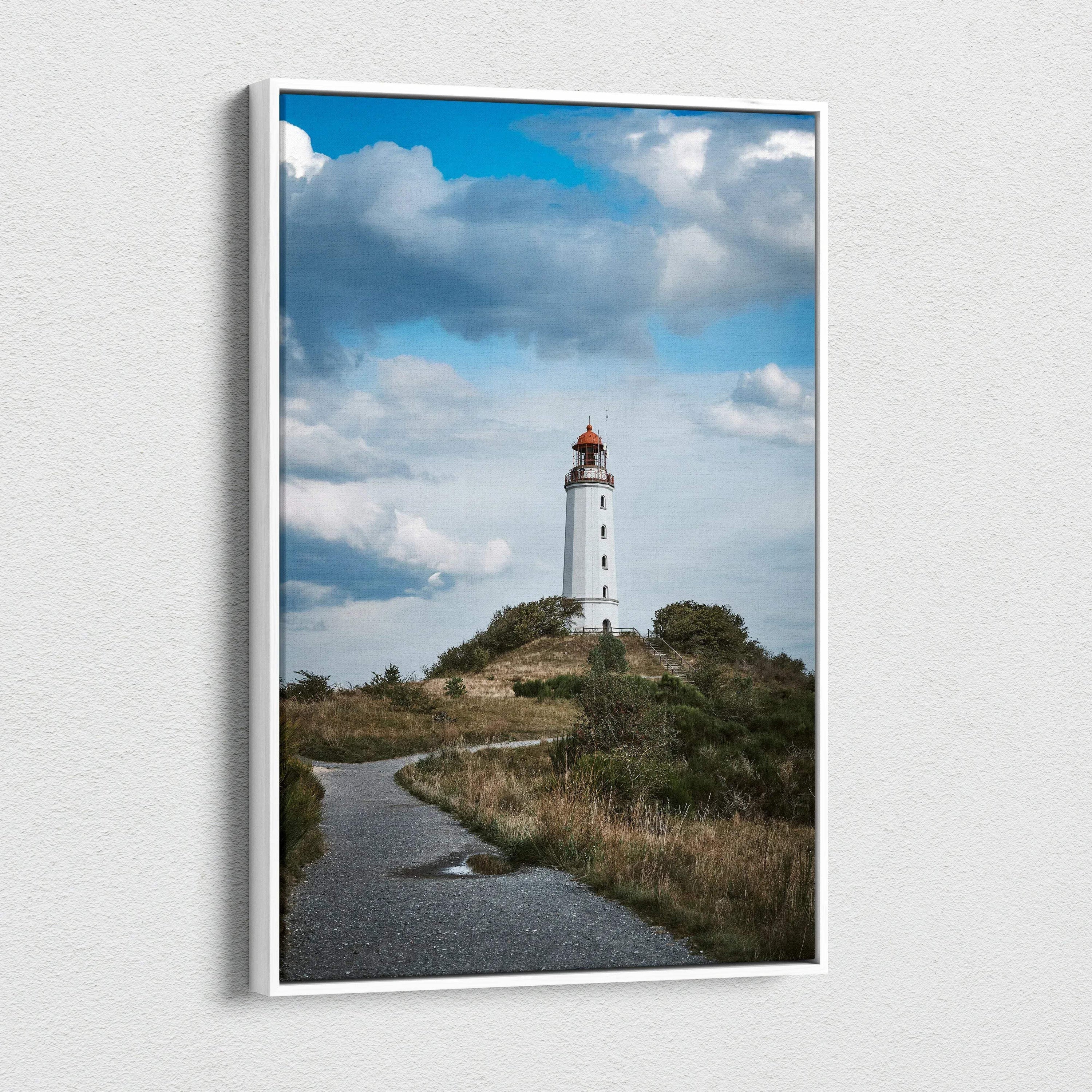 Vertical canvas wall art of a white lighthouse on a grassy hill under a blue sky with clouds.