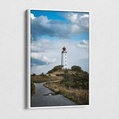 Vertical canvas wall art of a white lighthouse on a grassy hill under a blue sky with clouds.