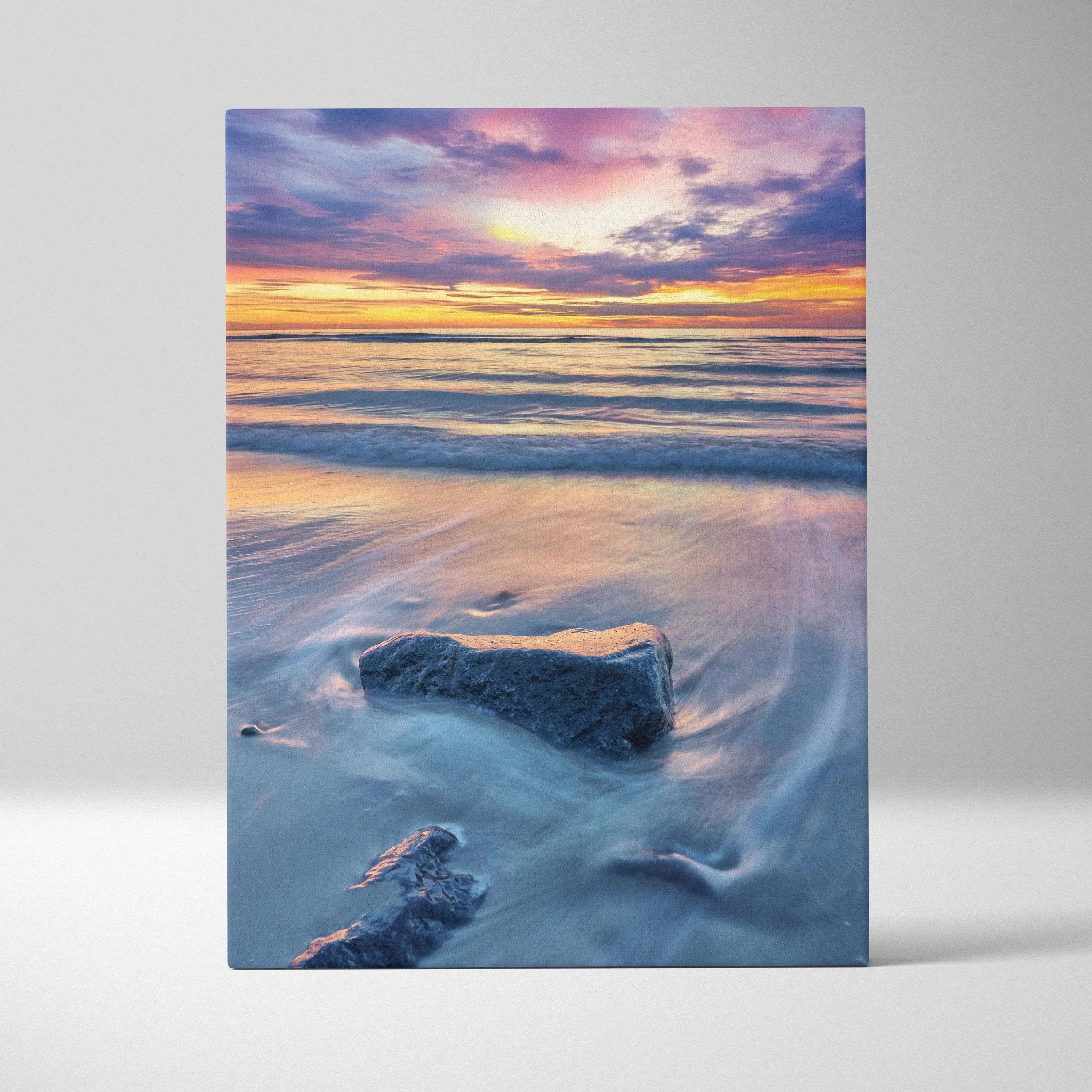 Canvas wall art of a tranquil beach sunset with soft pastel skies and waves flowing around rocks.