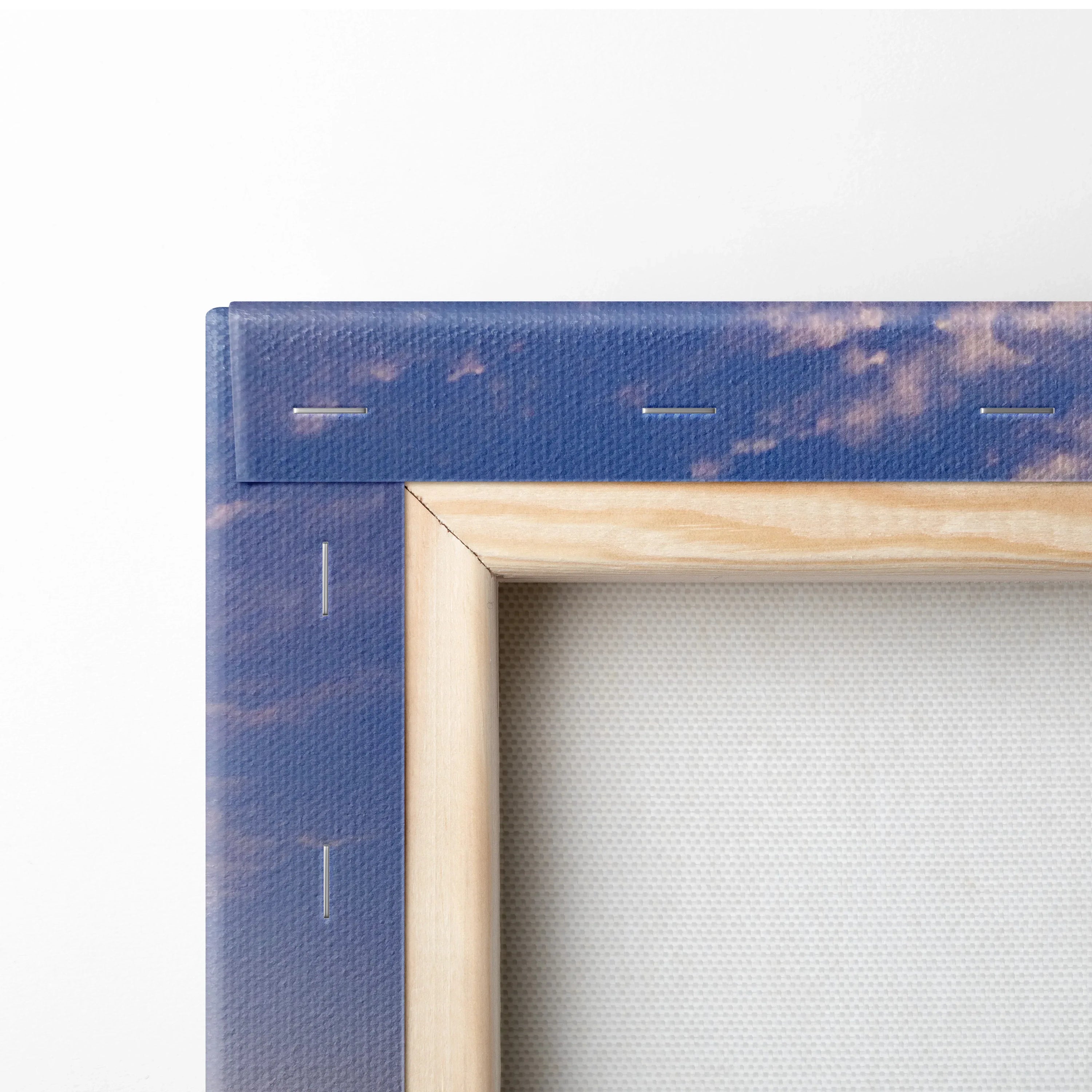 Close-up of wooden frame corner and staples on stretched canvas wall art with blue and purple sunset colors.
