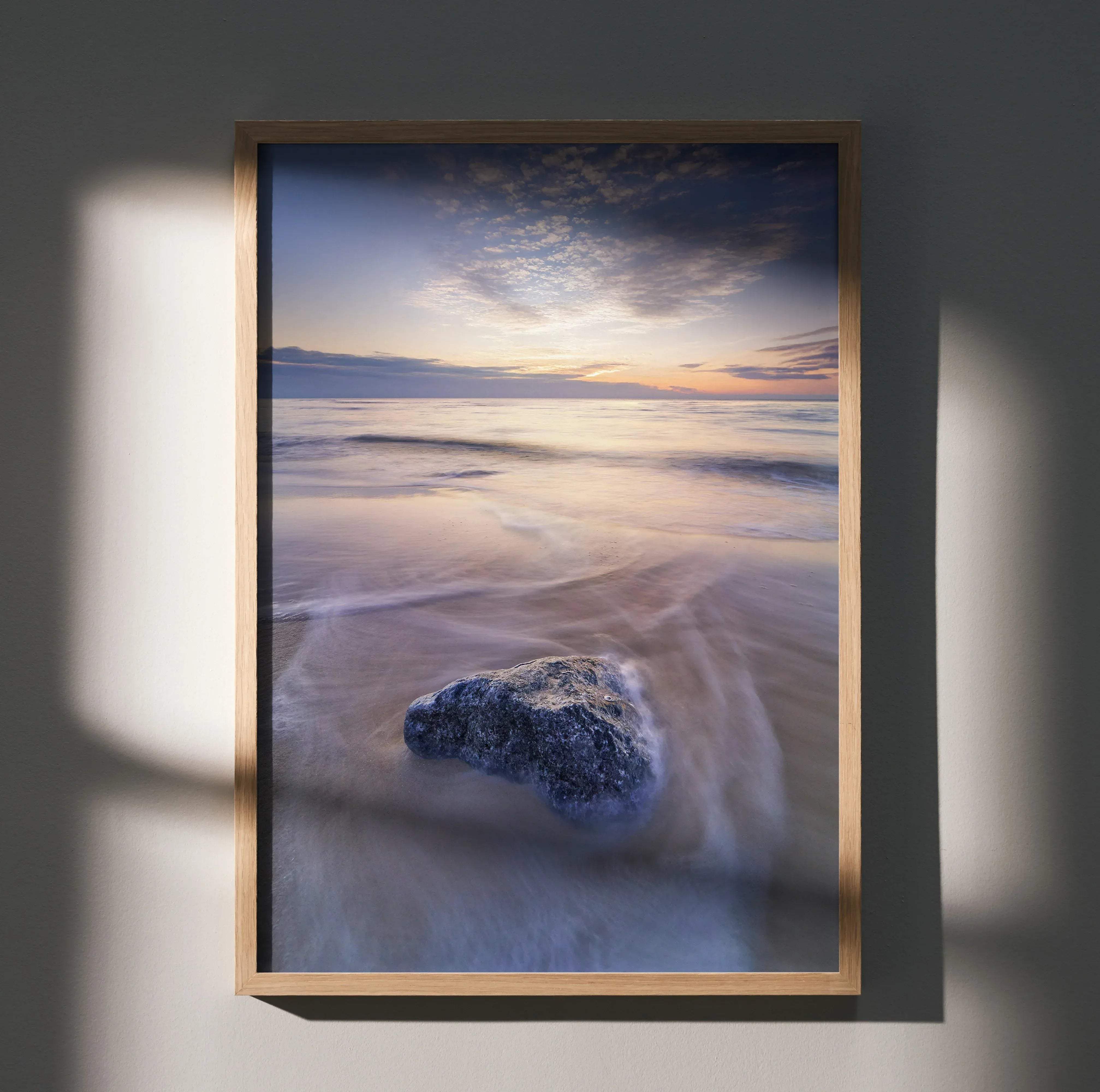 A vertical vibrant beach sunset ocean wall art poster featuring a dark gray rock on wet sand with soft waves and gradient sky