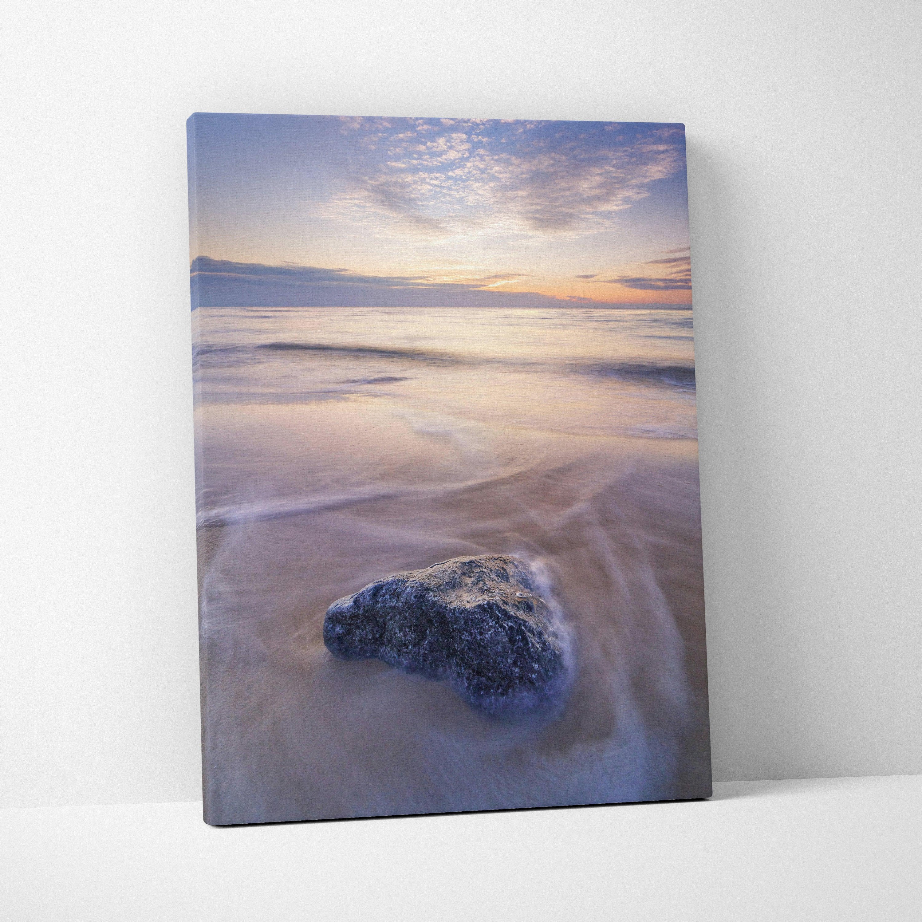 Serene beach sunset canvas wall art with soft pastel sky and gentle ocean waves over a smooth rock.
