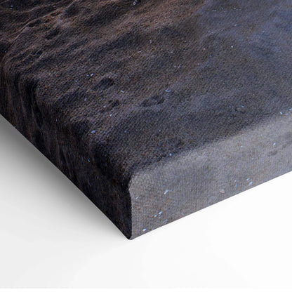 Close-up of textured canvas wall art showing dark sand and subtle water reflections from a beach sunset scene.