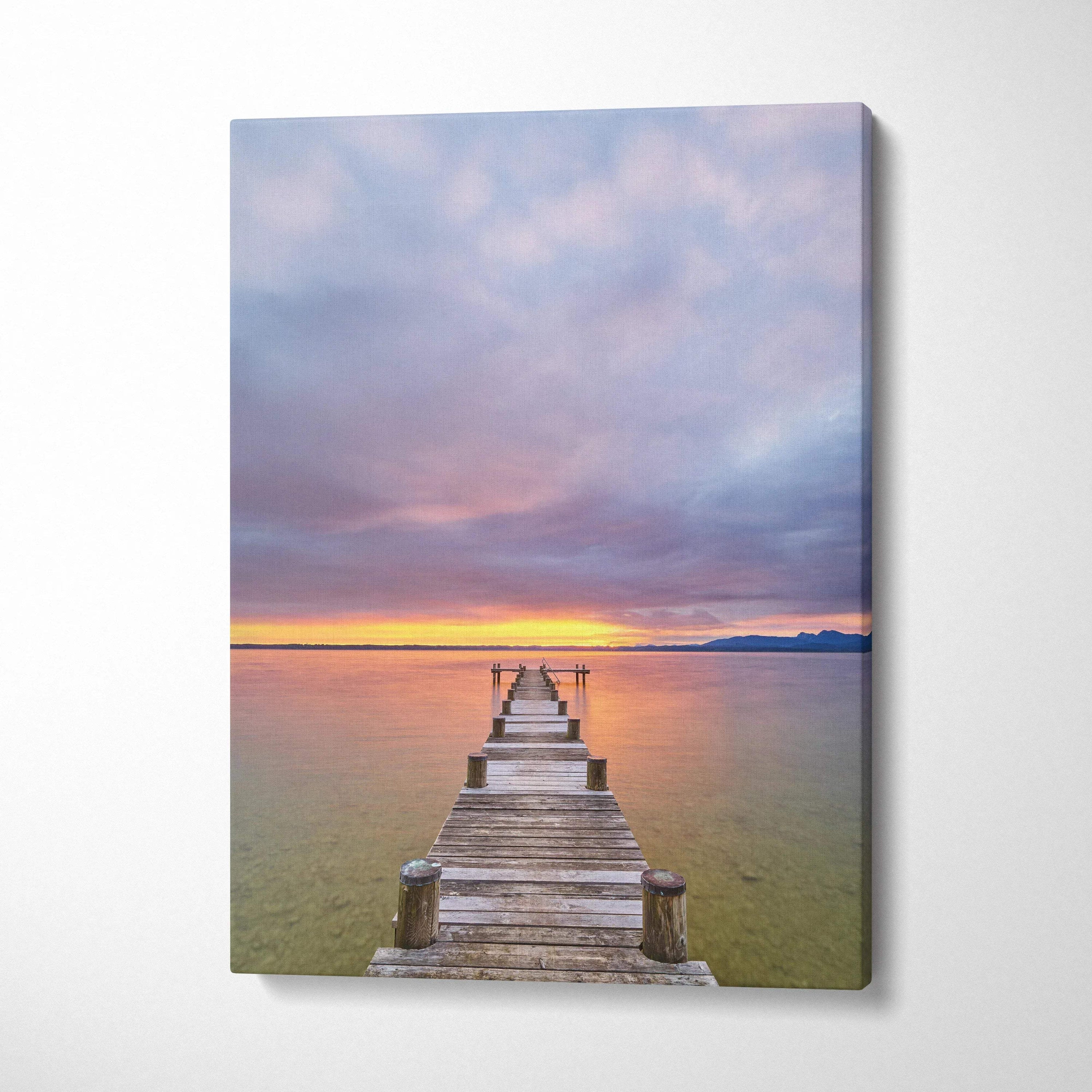 Canvas wall art of a wooden pier leading to a colorful vibrant beach sunset with clouds over calm water.