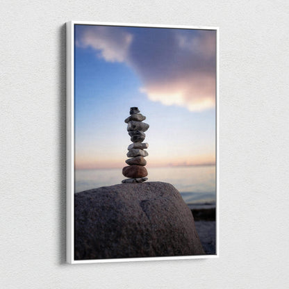 Vertical canvas wall art of stacked stones on a beach with a colorful sunset sky.