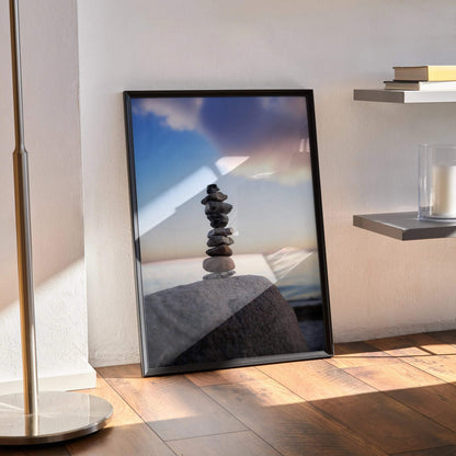 Serene nature landscape wall art poster with stacked stones and soft sky in black frame, vertical orientation.
