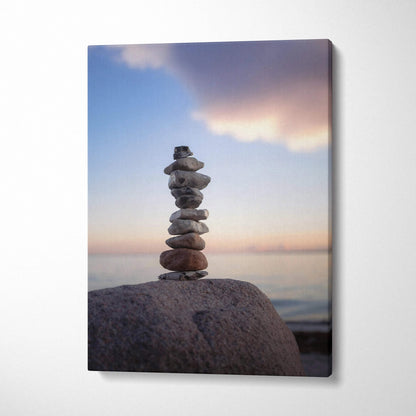 Canvas wall art featuring a serene stack of balanced beach stones at sunset with soft clouds and calm water background.
