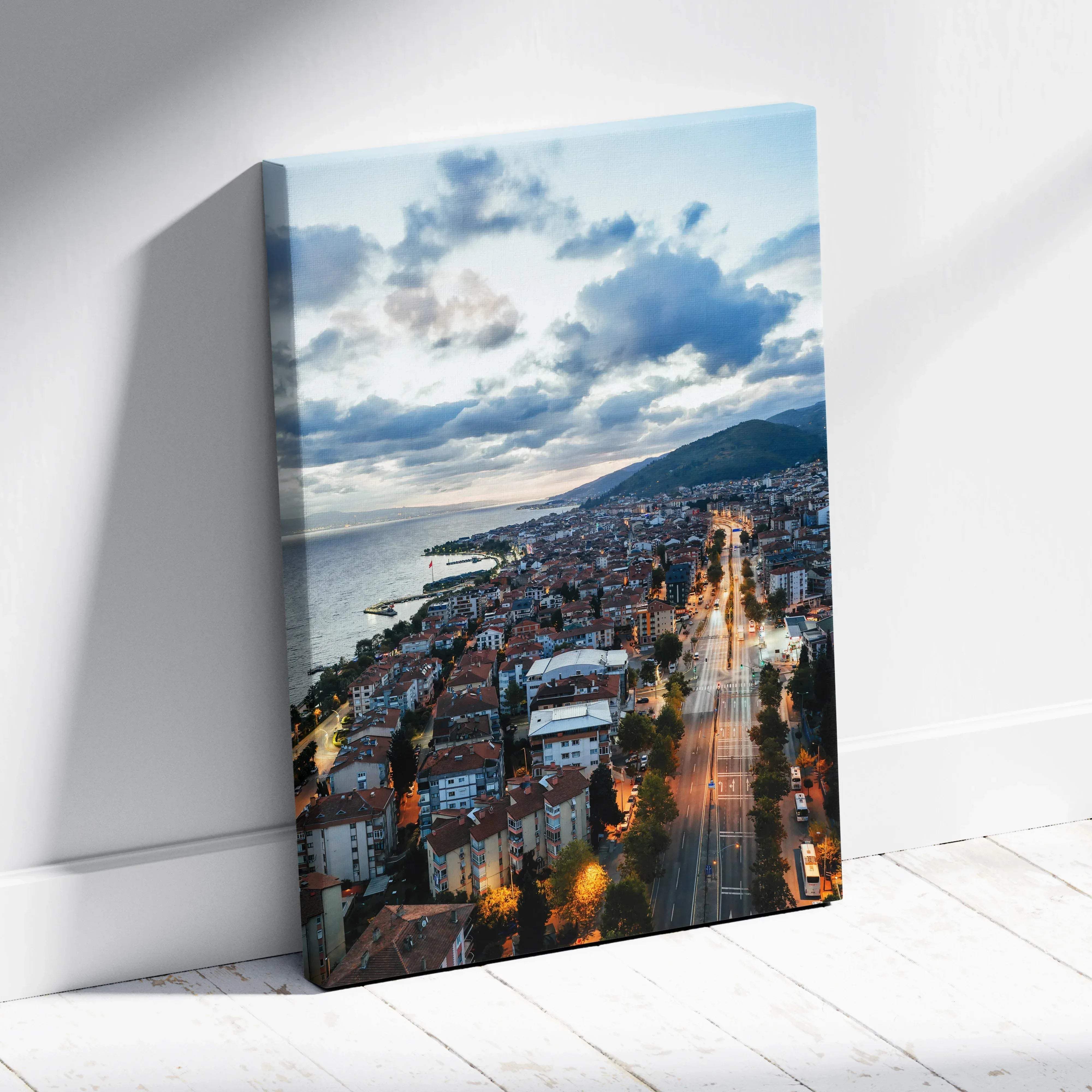 A rectangular canvas print of a coastal cityscape at dusk with illuminated streets and dramatic blue clouds