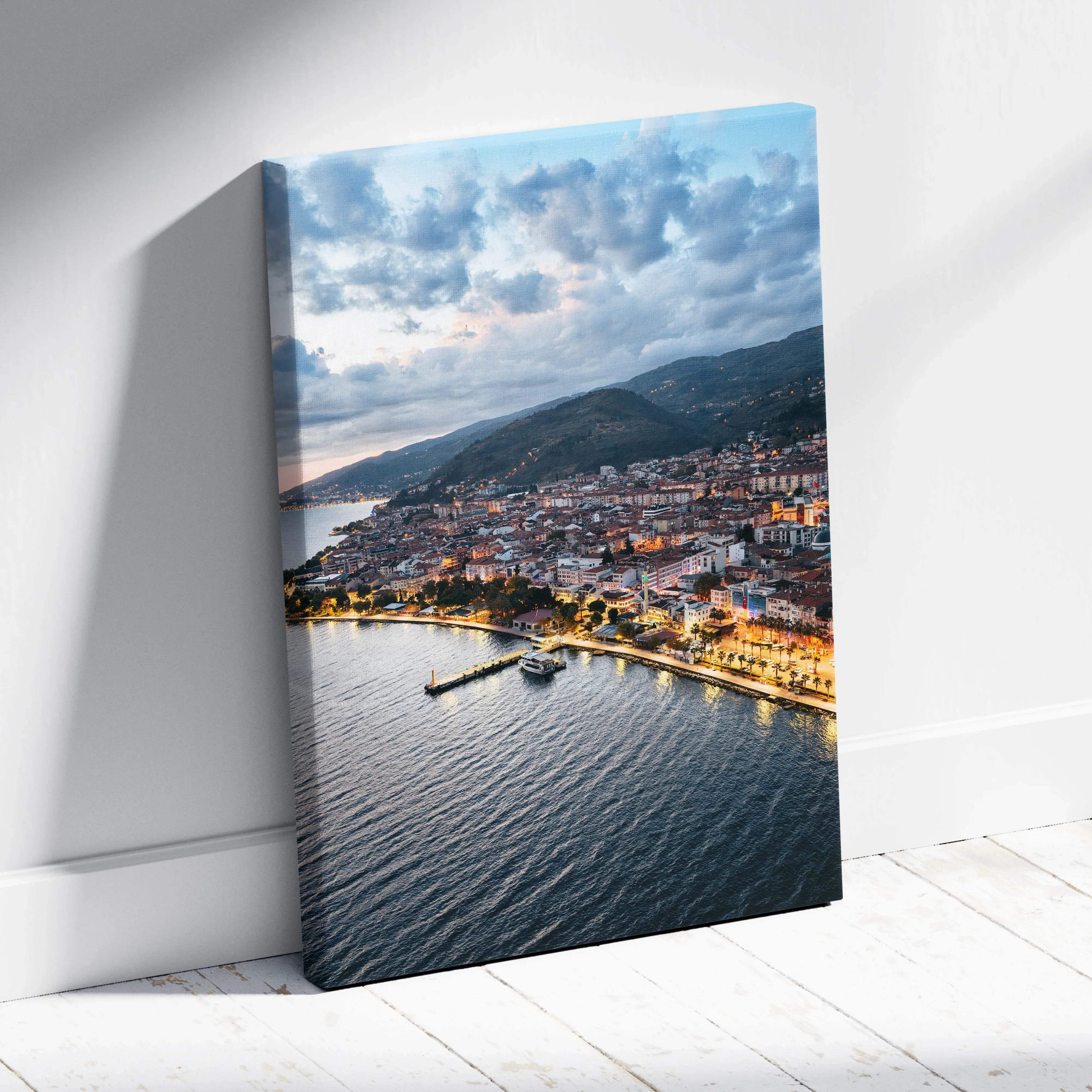 A framed canvas print of a coastal town harbor at dusk with warm golden hour glow and illuminated waterfront buildings