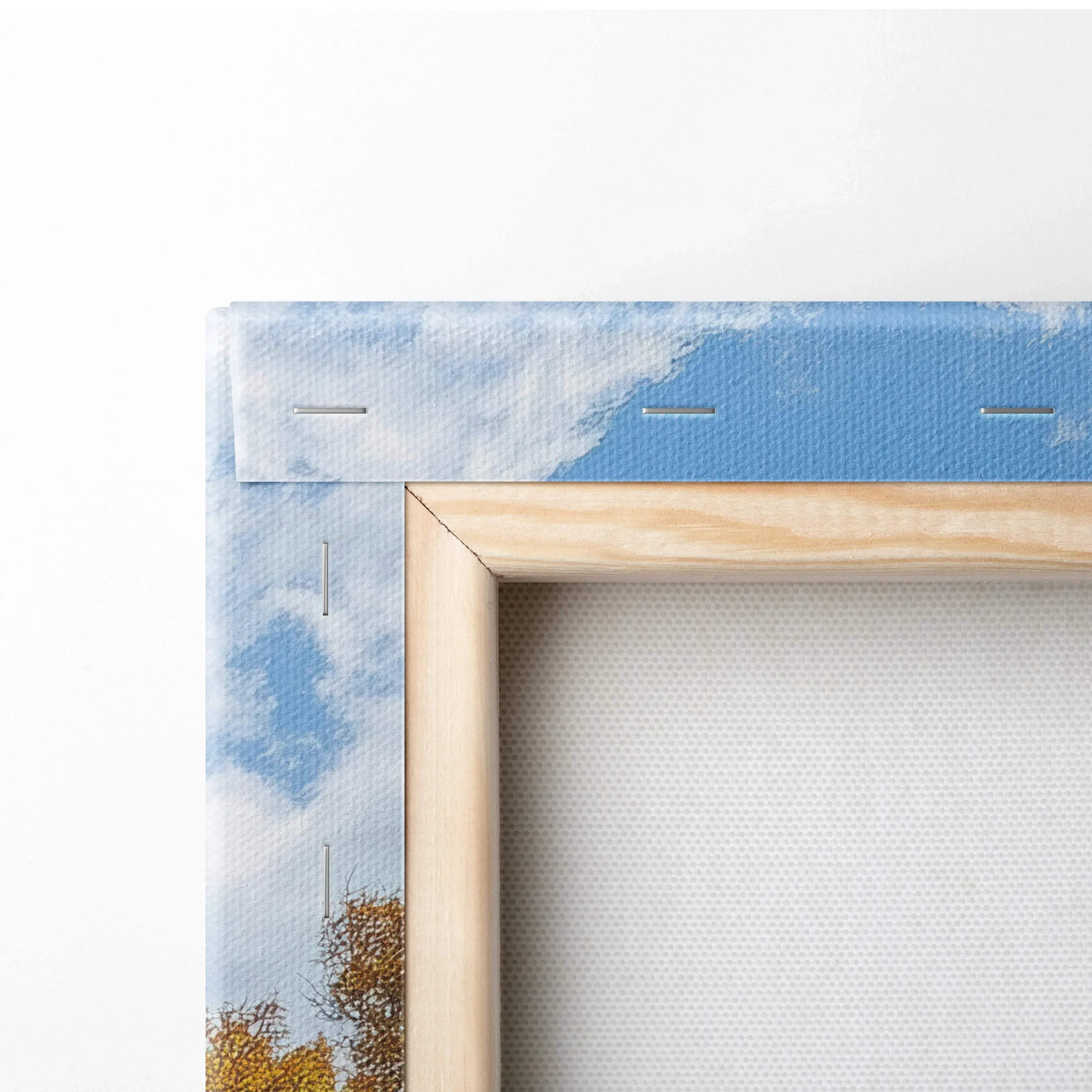 Close-up of wooden frame corner and canvas edge with blue sky and autumn trees printed on canvas wall art.