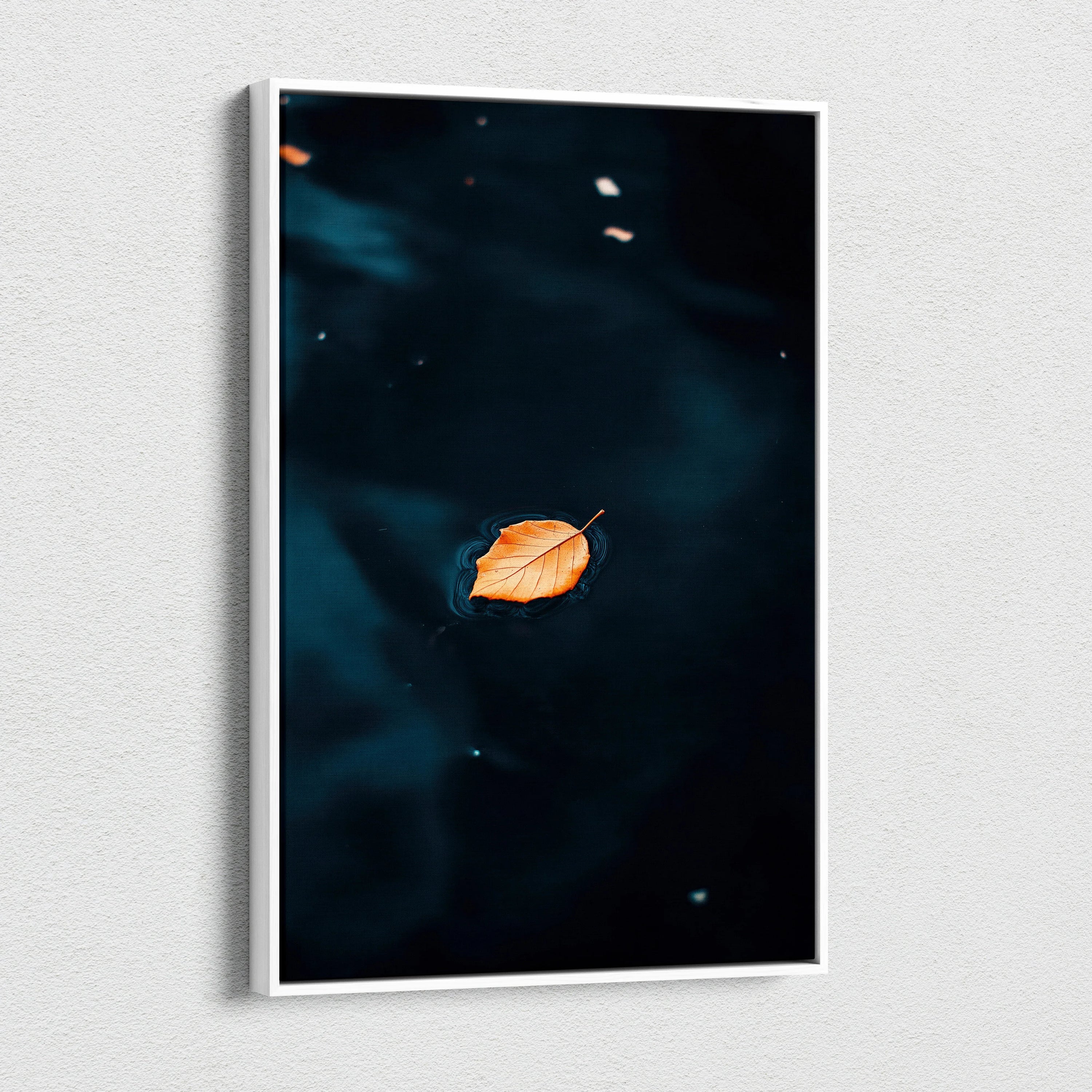 Minimalist autumn leaf floating on dark water canvas wall art print in vertical white frame.