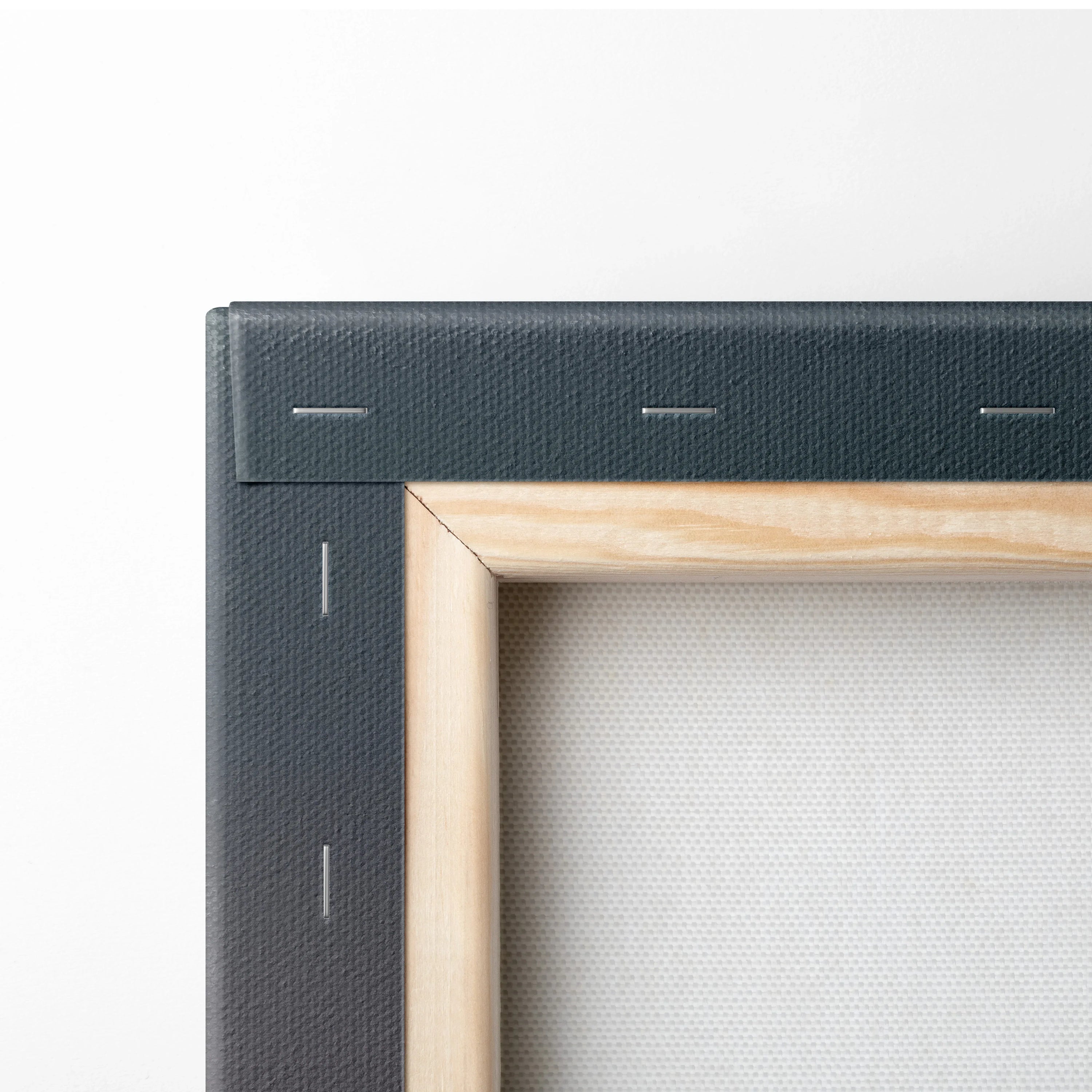 Close-up of natural wood frame corner with black canvas backing and silver staples, wall art decor detail.