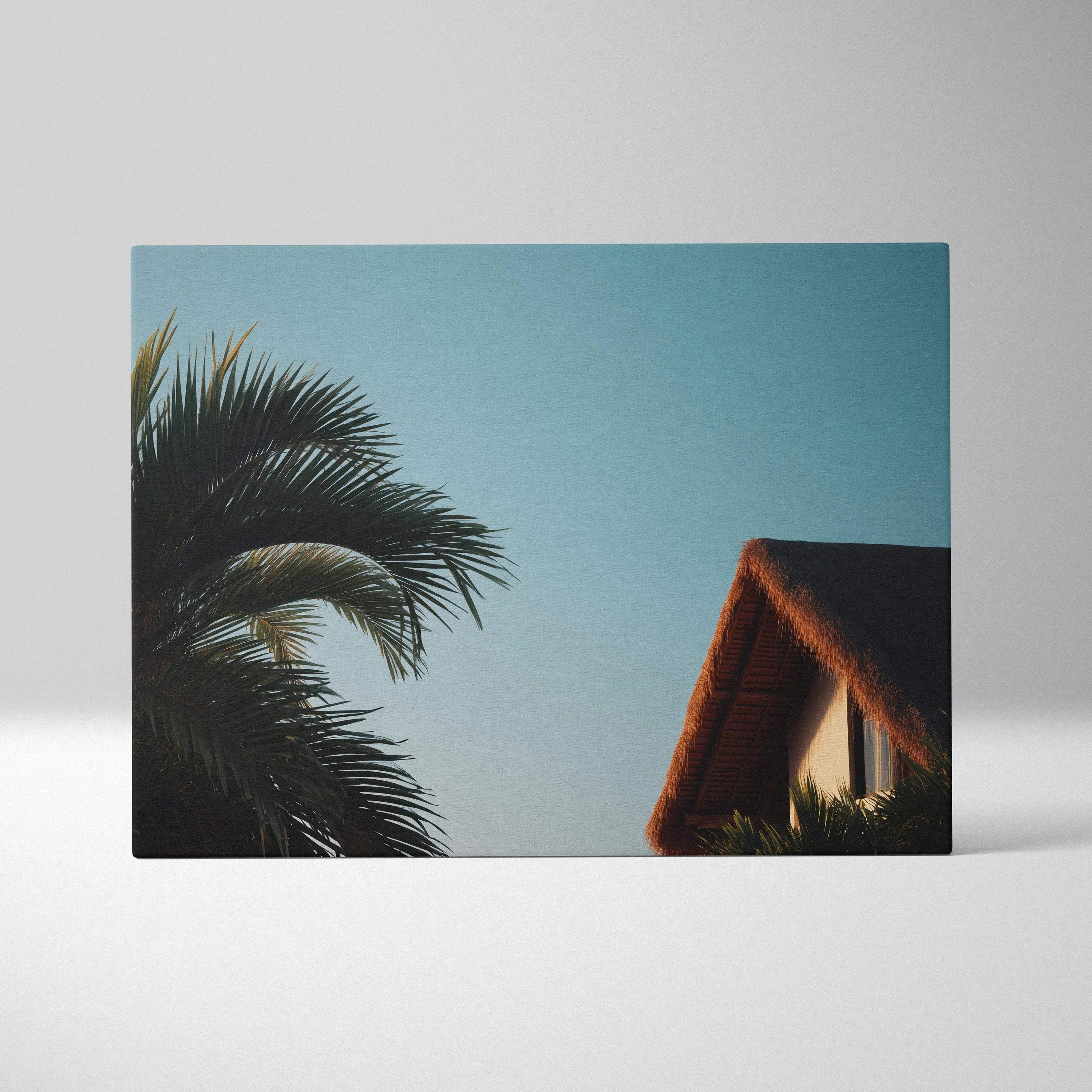 Canvas wall art featuring a tropical scene with dark green palm fronds and a thatched roof house under a clear blue sky.