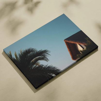 Canvas wall art featuring digital tropical scene with palm trees and a thatched roof house against clear blue sky.