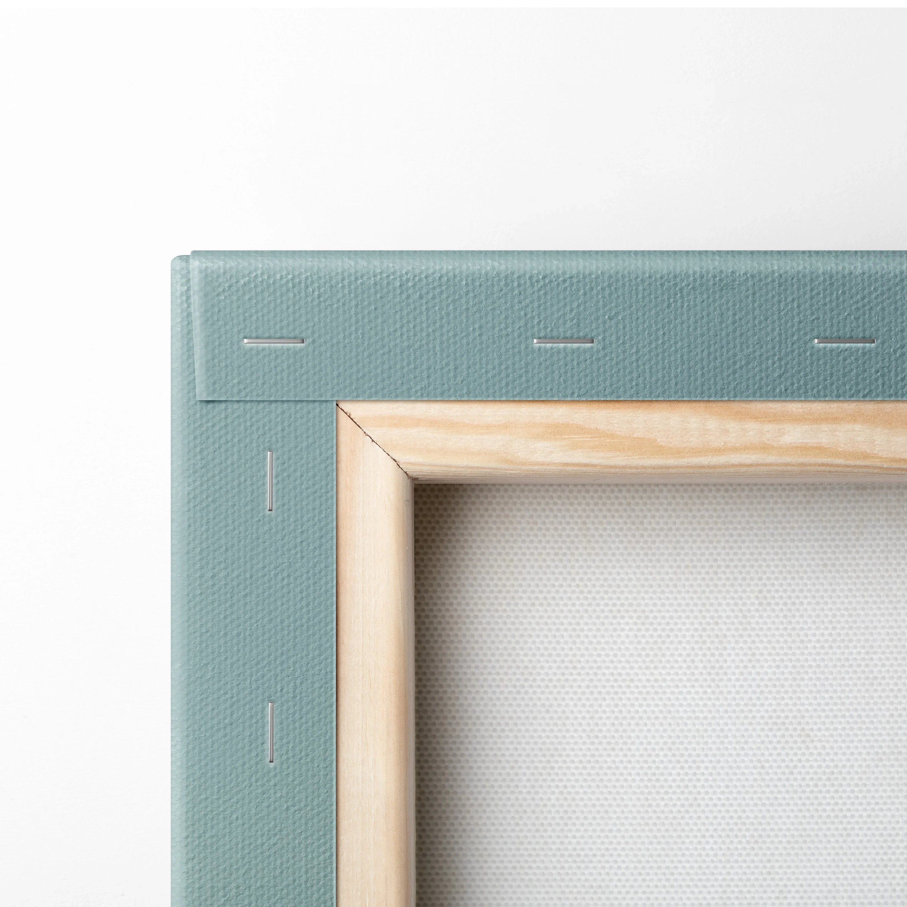 Close-up of stretched canvas corner with green fabric backing and natural wood frame, secured by staples.
