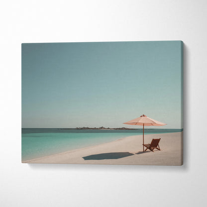 Canvas wall art of a tropical beach with turquoise water, sandy shore, wooden chair, and pink umbrella decor.