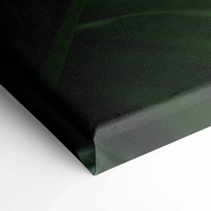 Close-up of canvas corner showing textured surface with dark green tropical leaf design and subtle sun flare effect in wall.