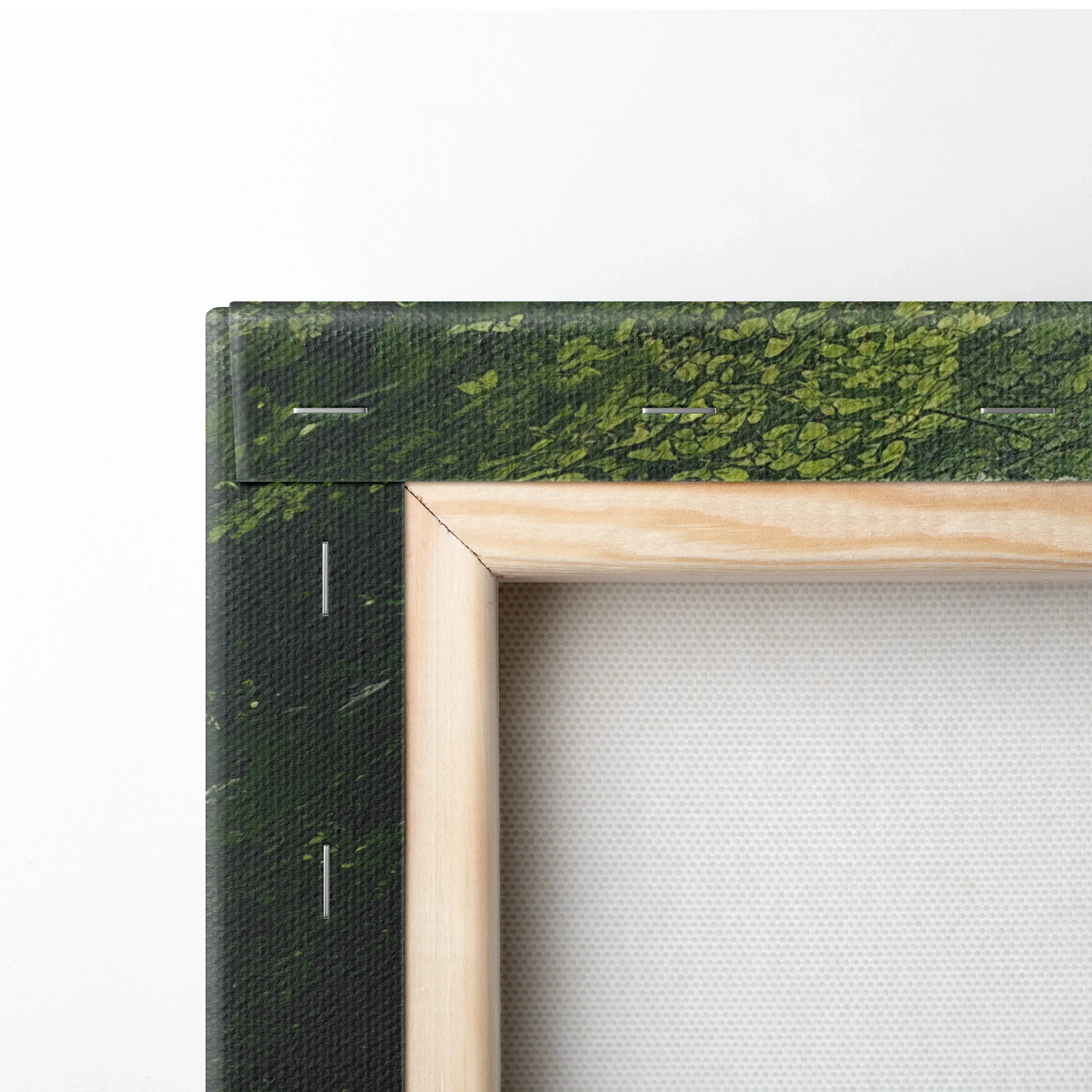 Corner of a stretched canvas wall art with a wooden frame and green forest print wrapping the edges.