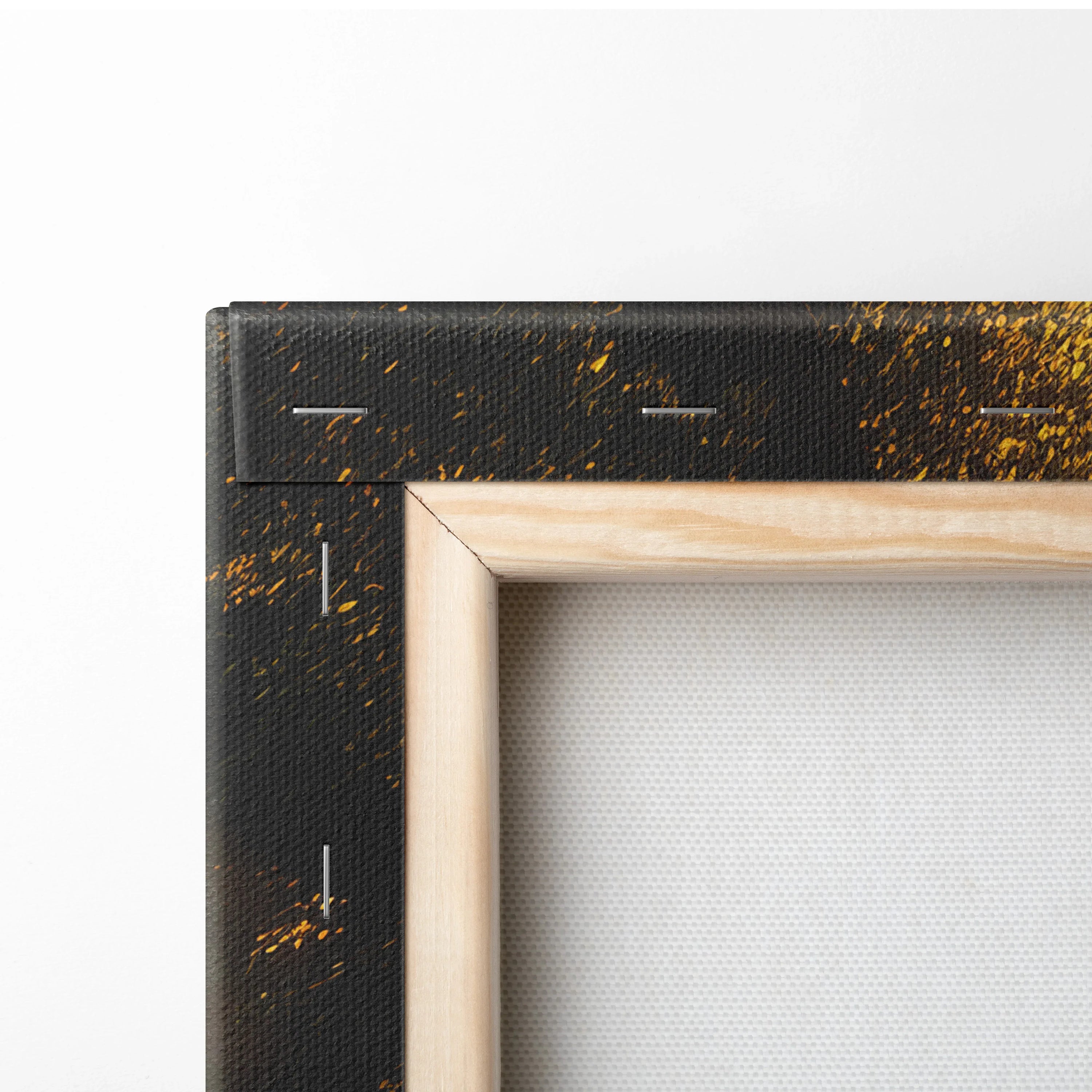 Close-up of wooden frame corner on black canvas wall art with golden paint splatters decor.