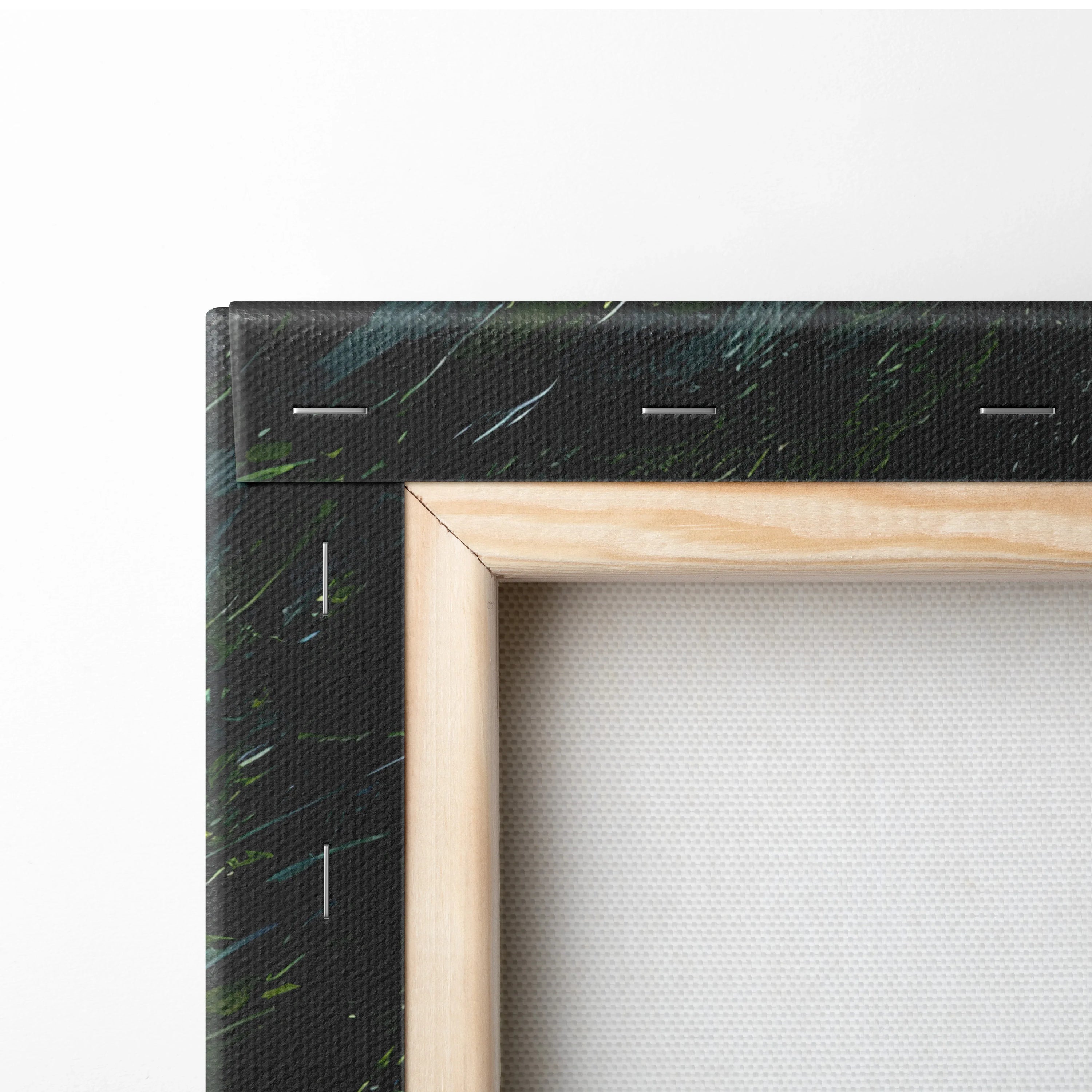 Corner close-up of black canvas with green and white streaks, wooden frame edge, blank white stretched backing.