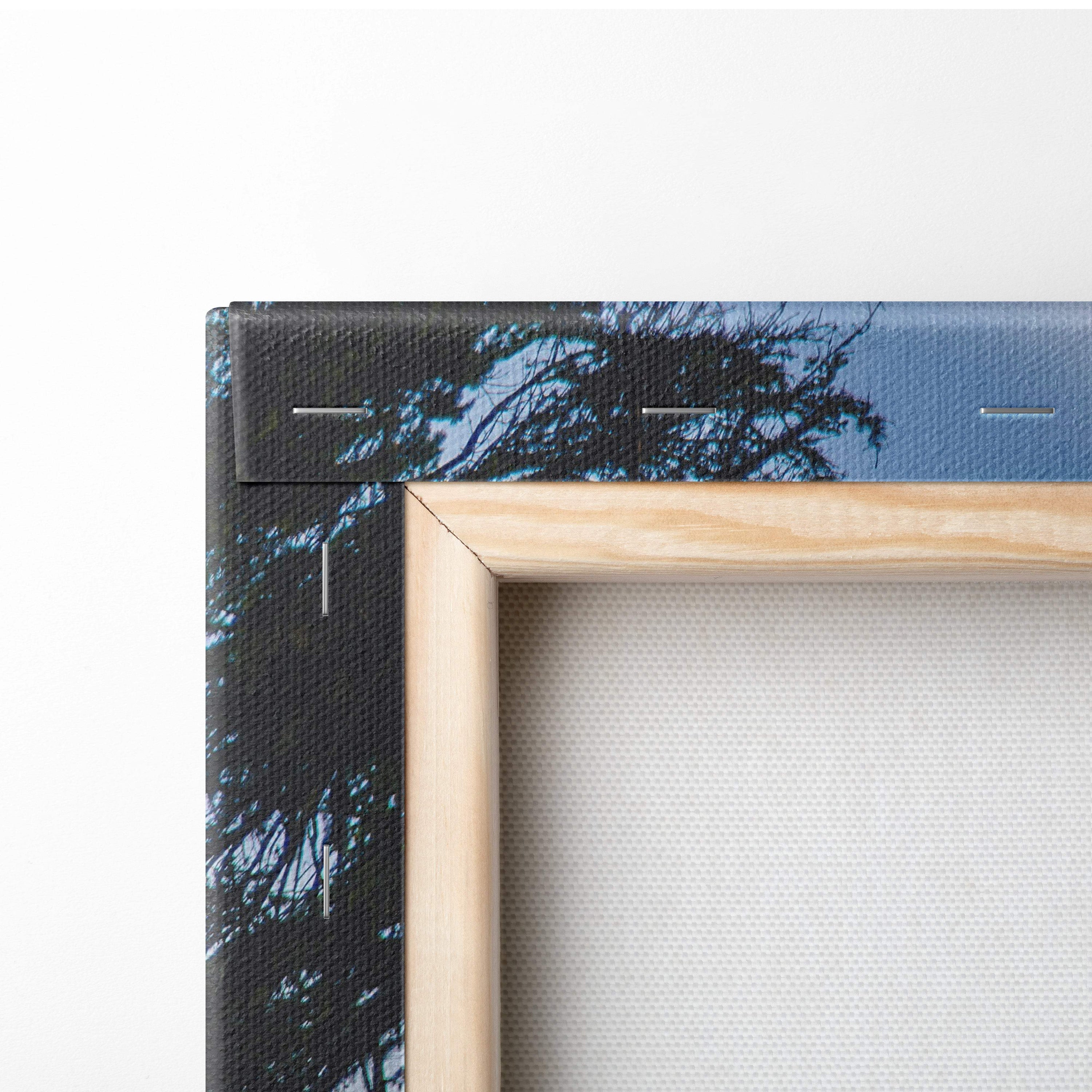 Light-colored wooden frame with canvas print of dark tree silhouettes against blue sky green blue mountain lake decor