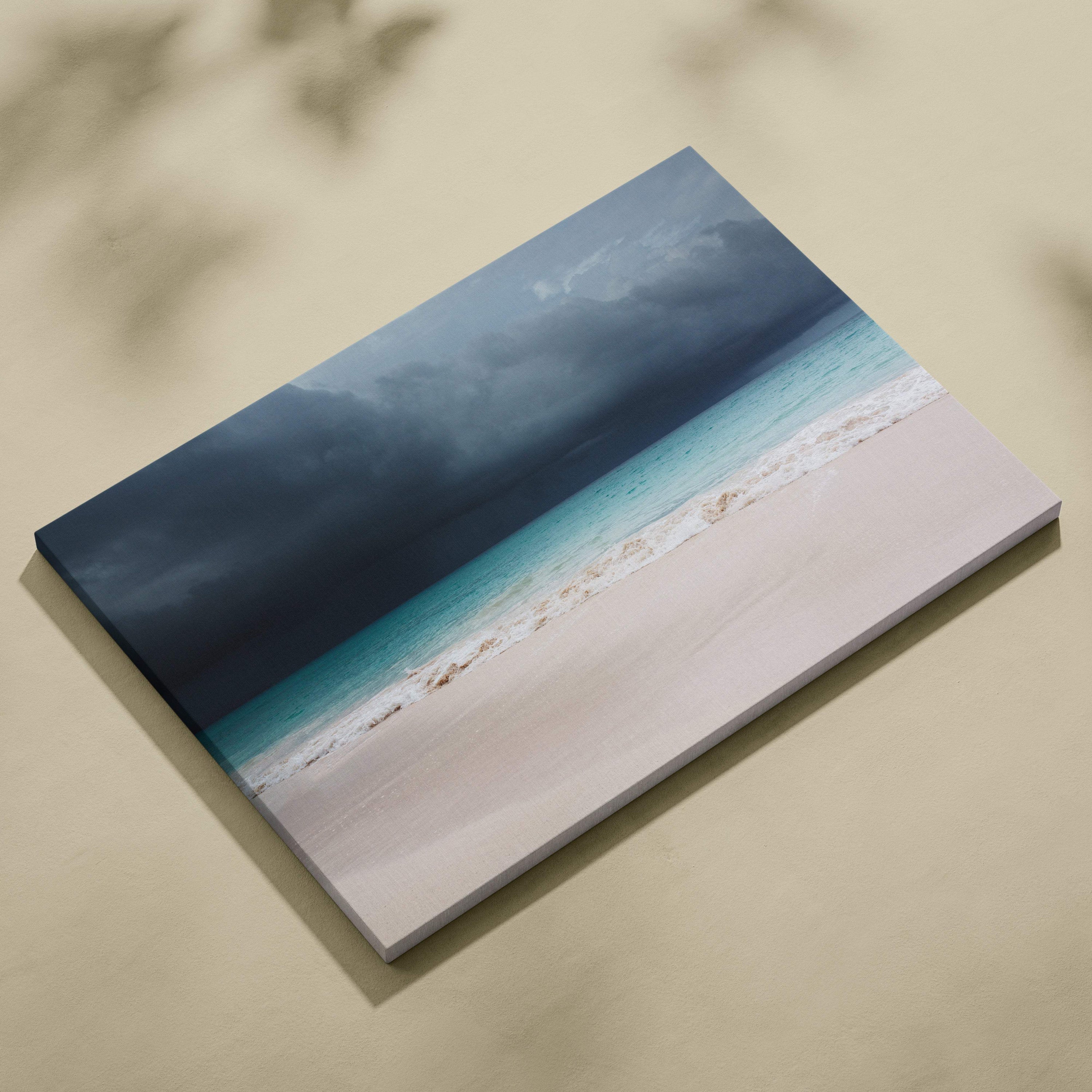 A rectangular canvas print of a stormy beach with turquoise waves and dark thunderclouds on pale sand coastal decor